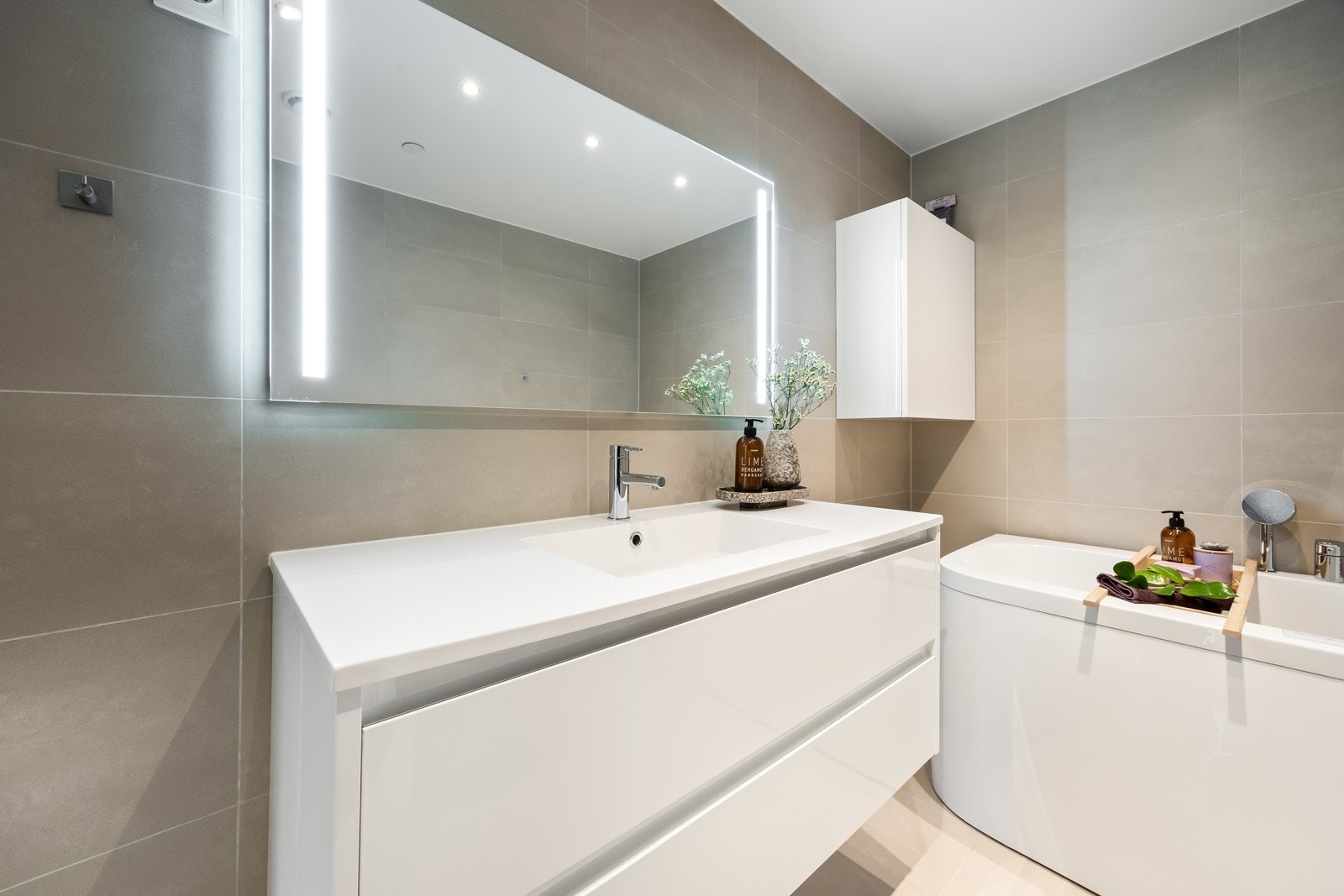 Badet er innredet med servantinnredning, speil med lys på vegg over servant, vegghengt toalett og boble badekar. Galleribilde