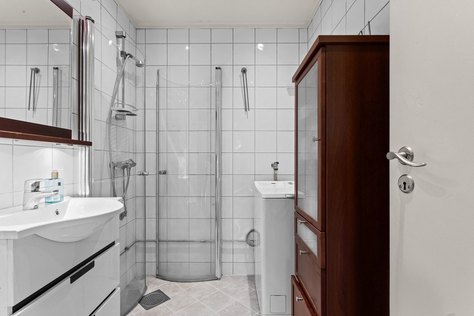 Badet er utstyrt med dusjsone med svingdører i glass, termostatstyrt blandebatteri, veggmontert klosett og servantskap med glatte fronter og heldekkende servant. Galleribilde