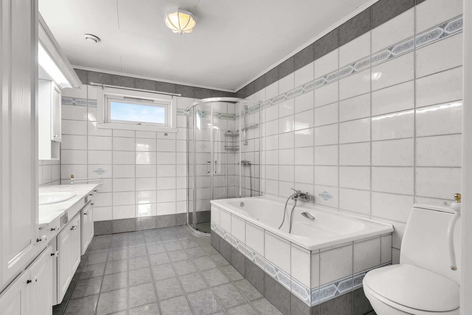 Badet i hovedetasjen har fliser på gulv og vegger, samt innredning med dusjhjørne, badekar, toalett og servant. Galleribilde