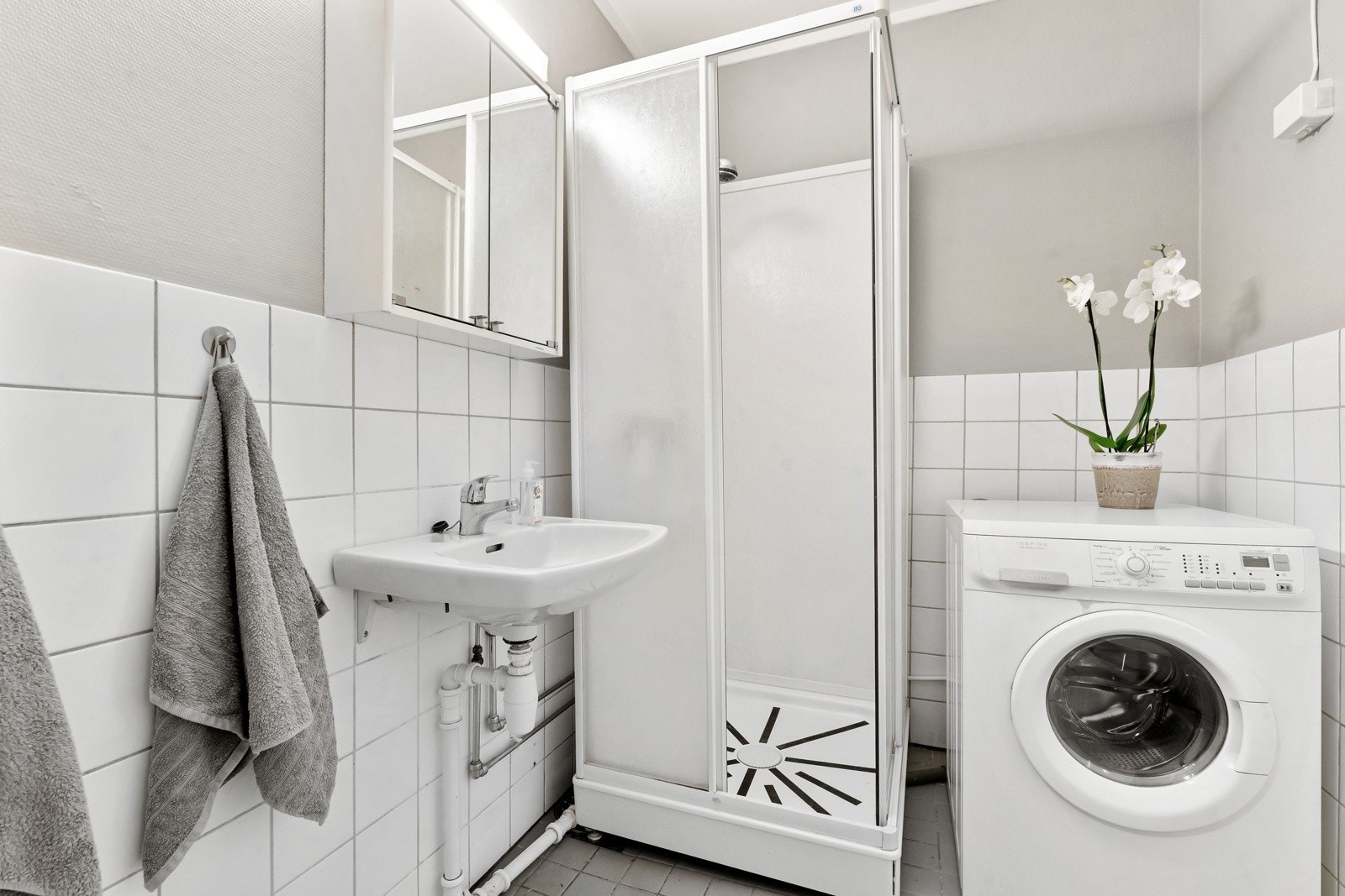 Flislagt baderom som består av dusjkabinett, vegghengt servant og speil. Galleribilde