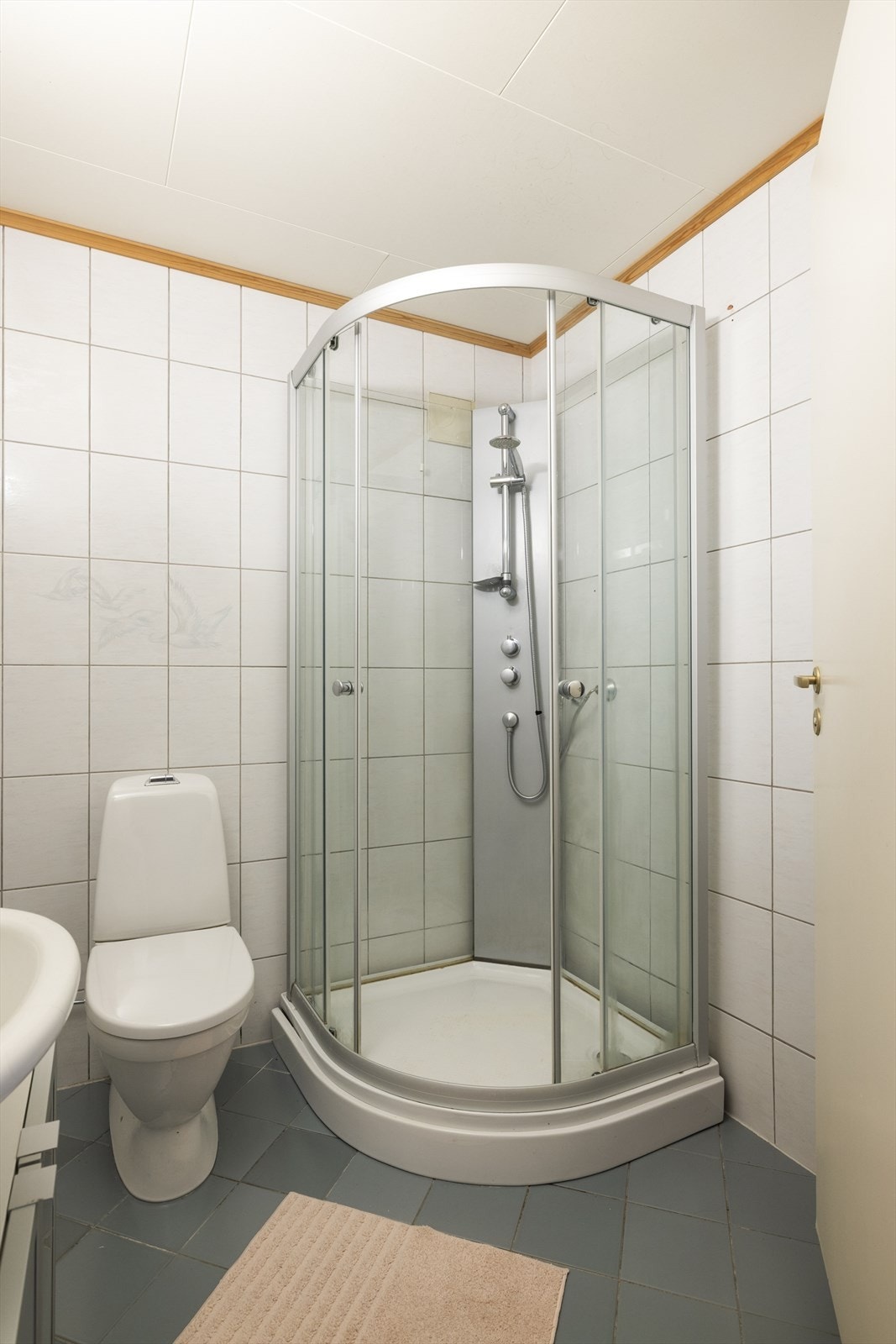 Det ene badet i underetasjen er innredet med klosett, servant på innredning, speilskap med lys og et praktisk dusjkabinett. Galleribilde