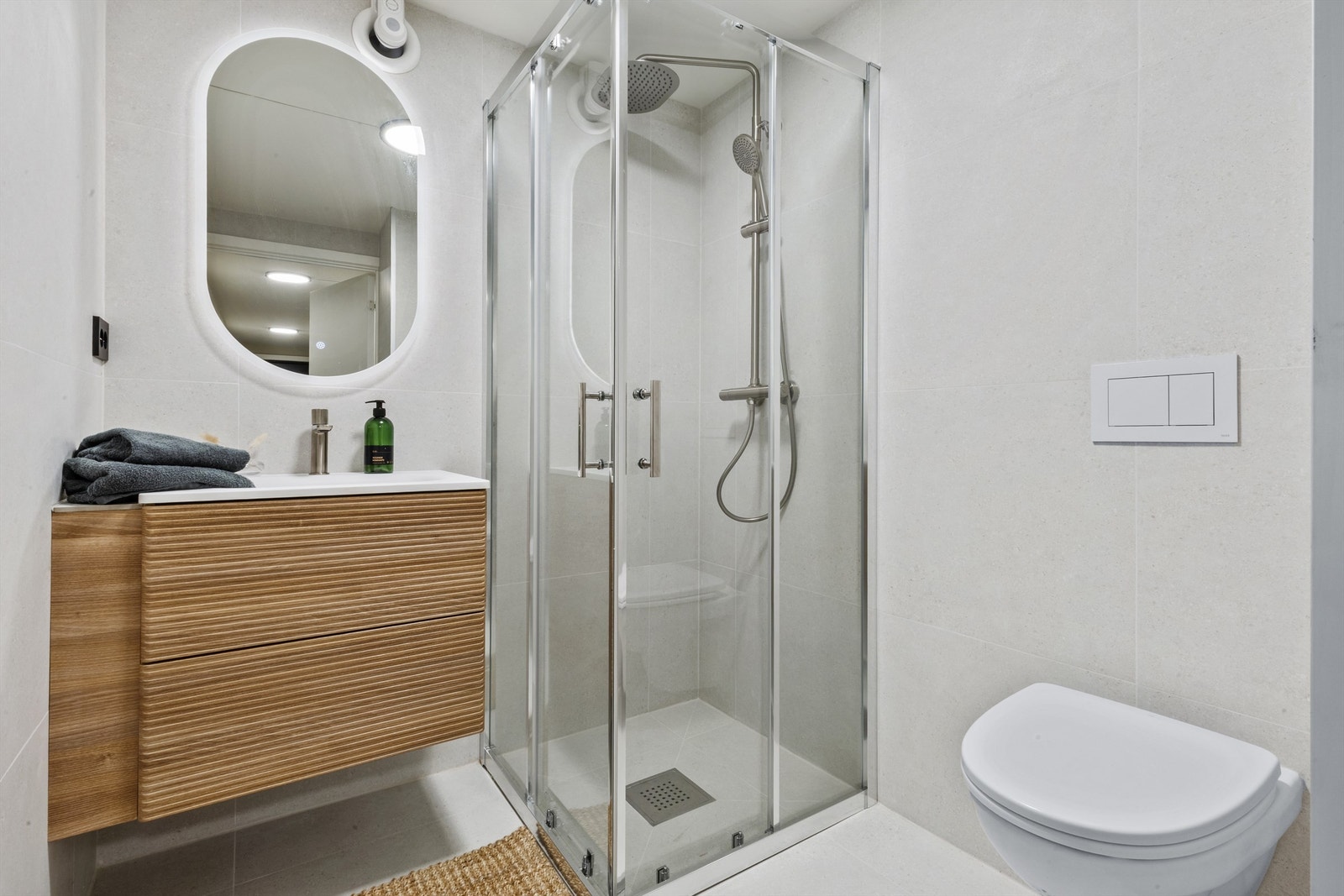 Lekkert flislagt bad med dusjnisje, vegghengt toalett, servant med oppbevaring og speil med touch-lys. Galleribilde