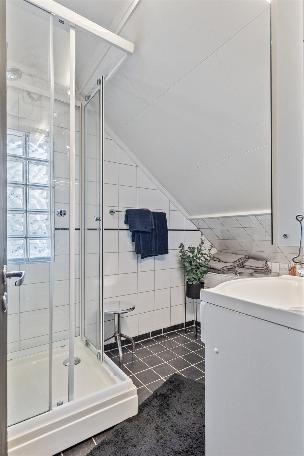 Badet har dusjkabinett med dører i glass, servant innfelt i servantskap og vindu med glassbygger stein. Galleribilde