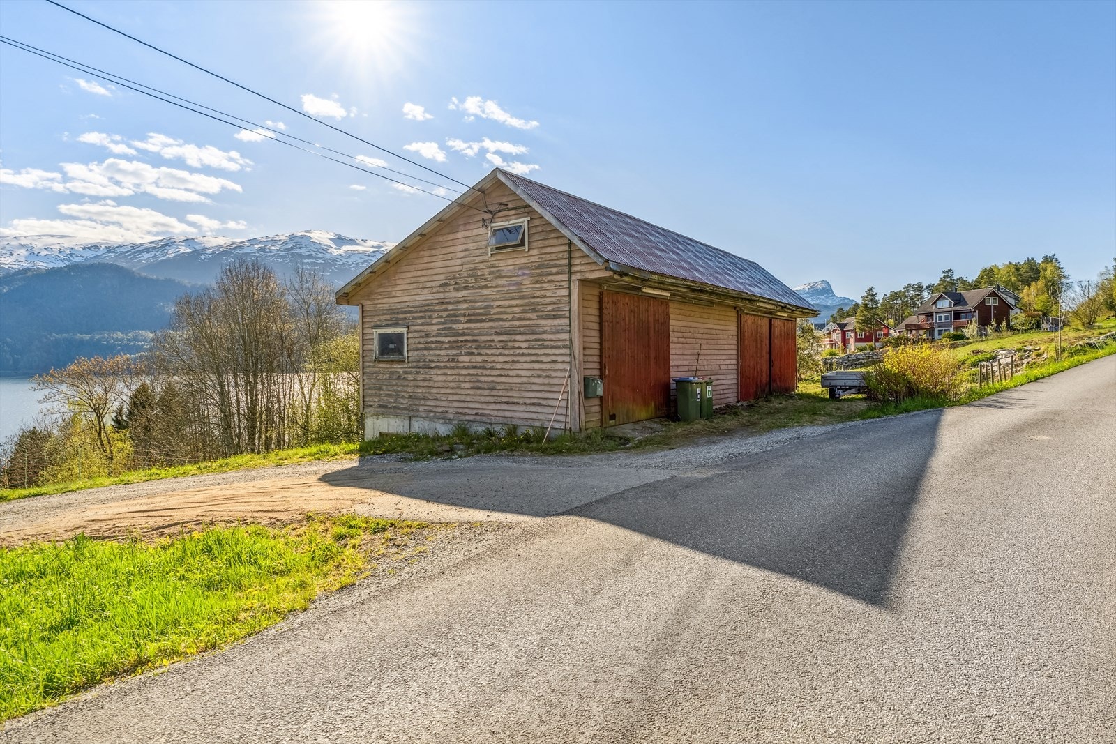 Praktisk garasjebygg/reiskapshus som ligg like ved innkøyrsla, med fleire glideportar i tre. Her har ein godt med plass til både køyretøy og lagring. Galleribilde