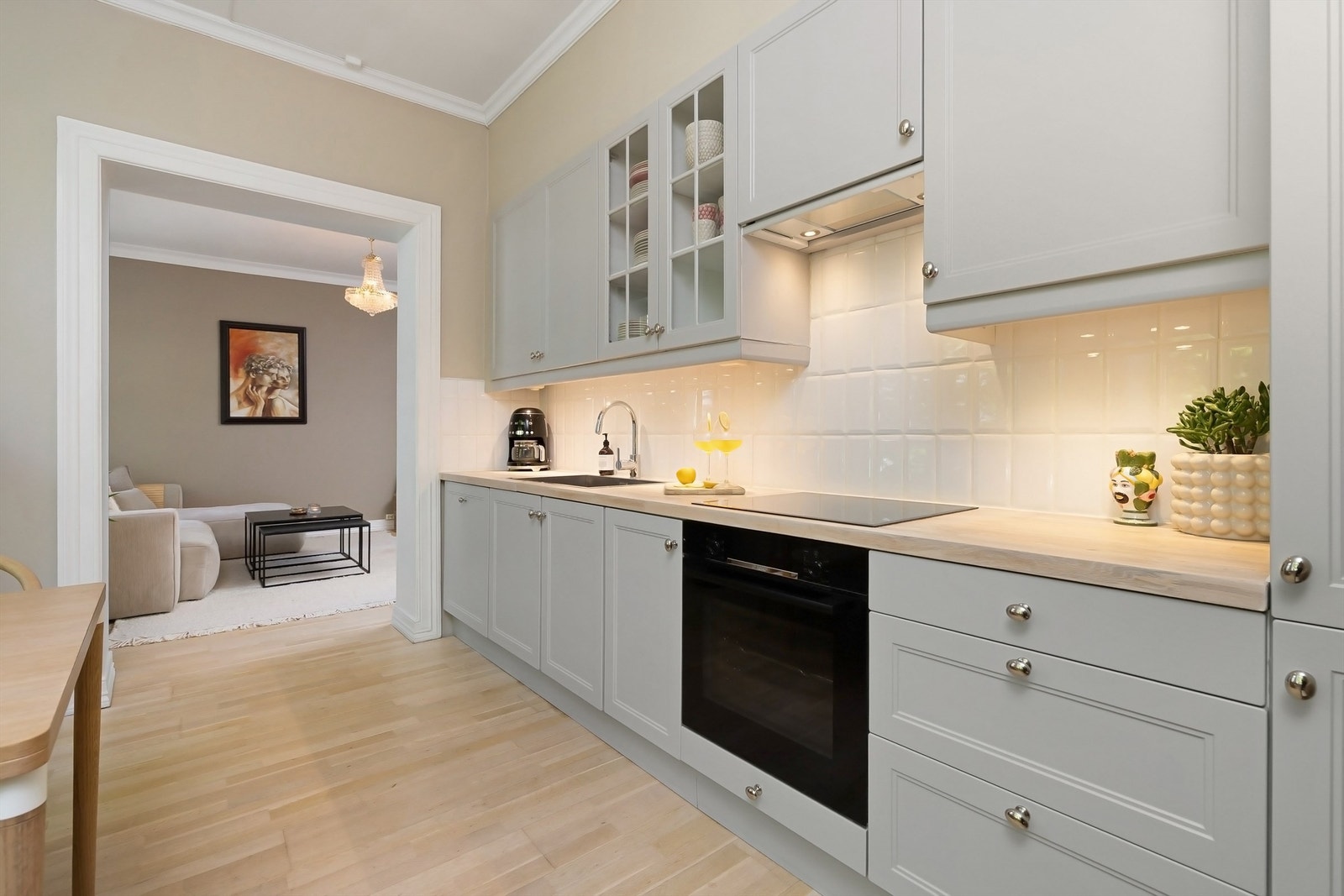 Lyst og tidløst kjøkken med gjennomgående parkett på gulv, samt lekre hvite fliser mellom benkeplate og overskap Galleribilde