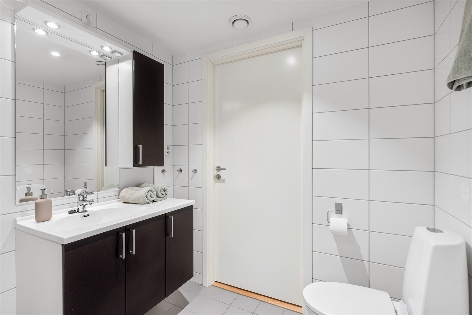 Sidekap med speilfront gir praktisk oppbevaring, mens servantskapet har stilrene, mørke fronter. Over servanten finner du speil med belysning. Galleribilde