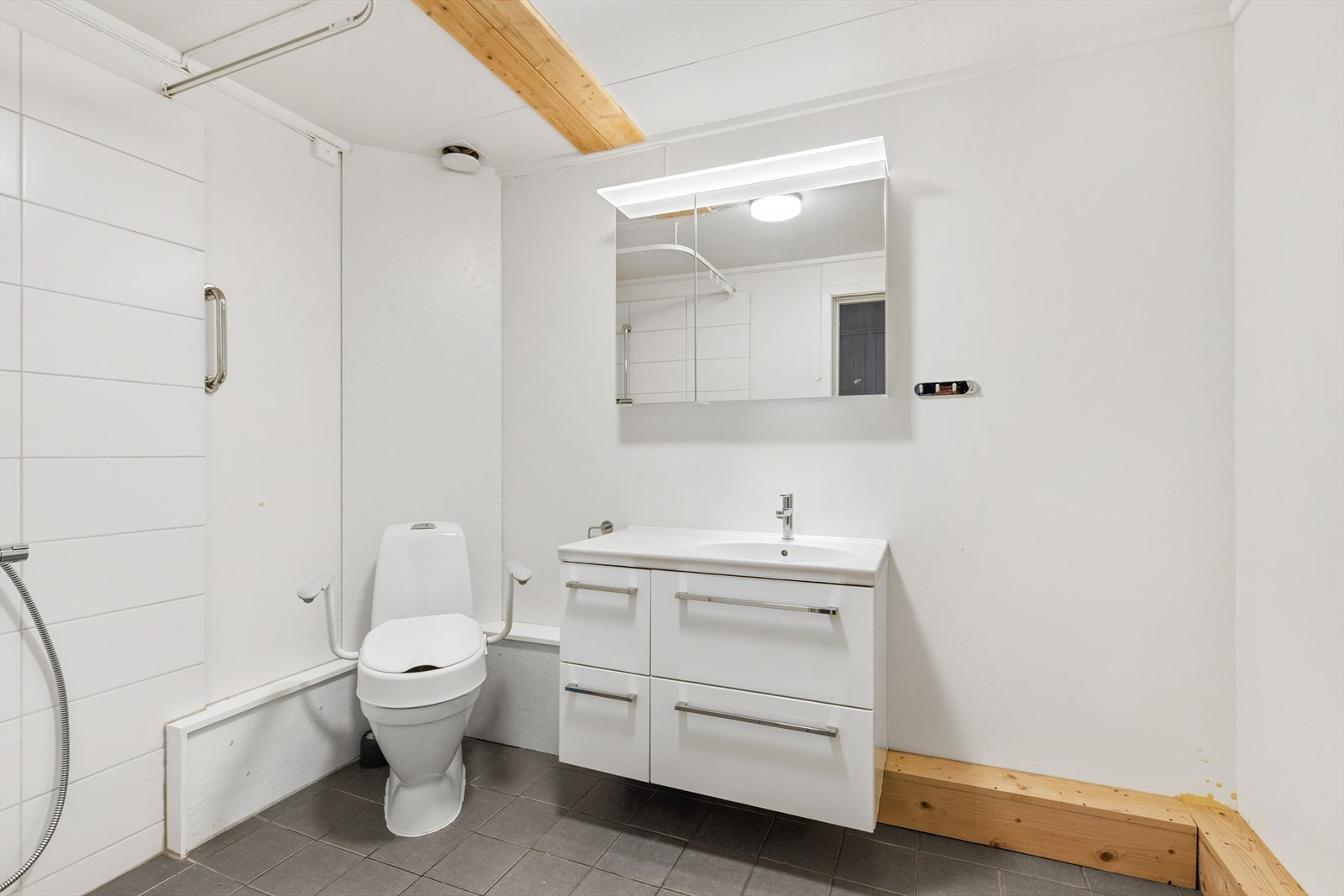 Bad med flislagt gulv, utstyrt med servant og dusjnisje. Speil og belysning i overkant av servant. Galleribilde