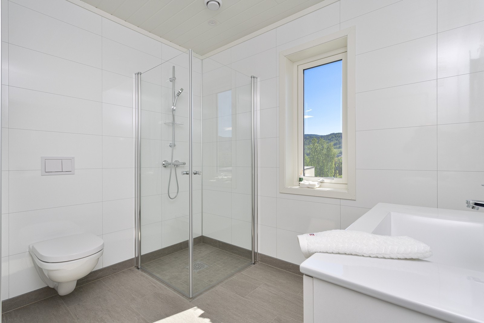 Badet inneholder vegghengt toalett, dusjhjørne med dusjvegger, servantinnredning med speil og opplegg for vaskemaskin. Galleribilde