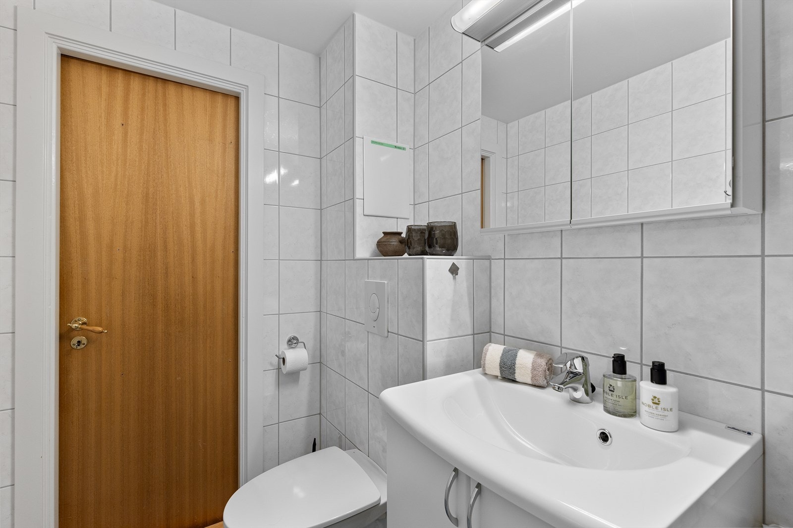 Det er veggmontert toalett i hvit porselen med totrinns vannspyling og innebygd sisterne. Galleribilde