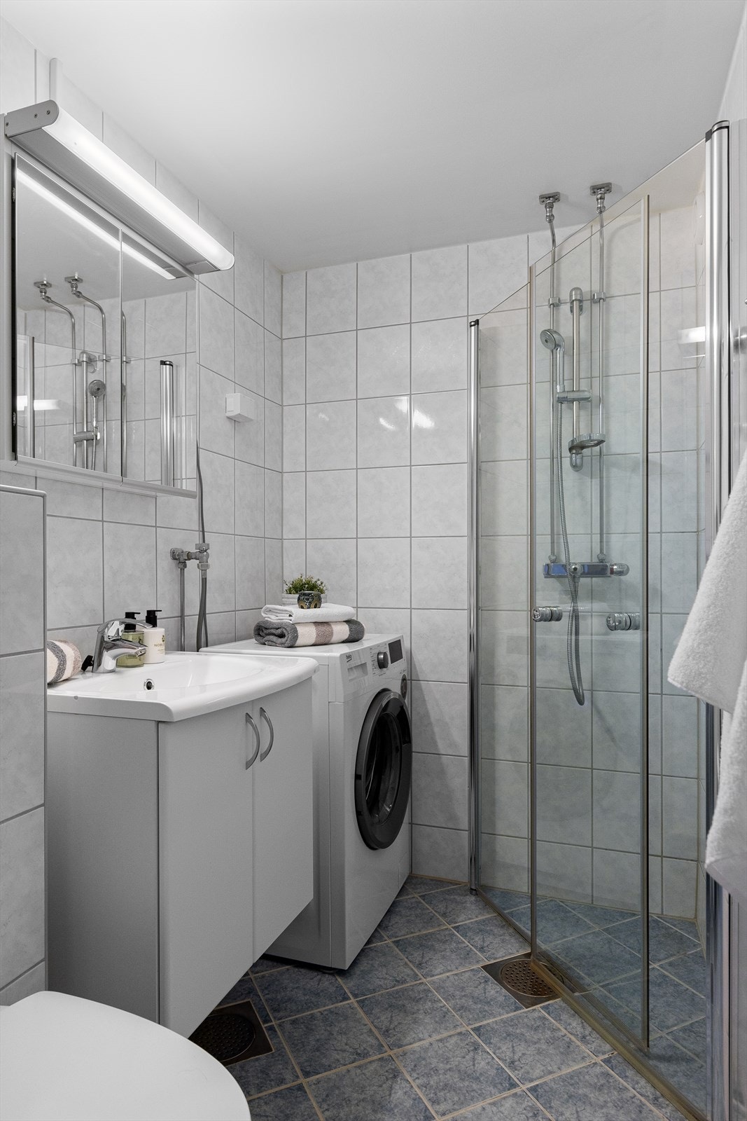 Servantskap med glatte hvite skapfronter. Speilskap med belysning over servant. Dusjhjørne med svingbare dusjdører av herdet glass, veggmontert dusjbatteri og dusjgarnityr med hånddusj. Opplegg for vaskemaskin. Galleribilde