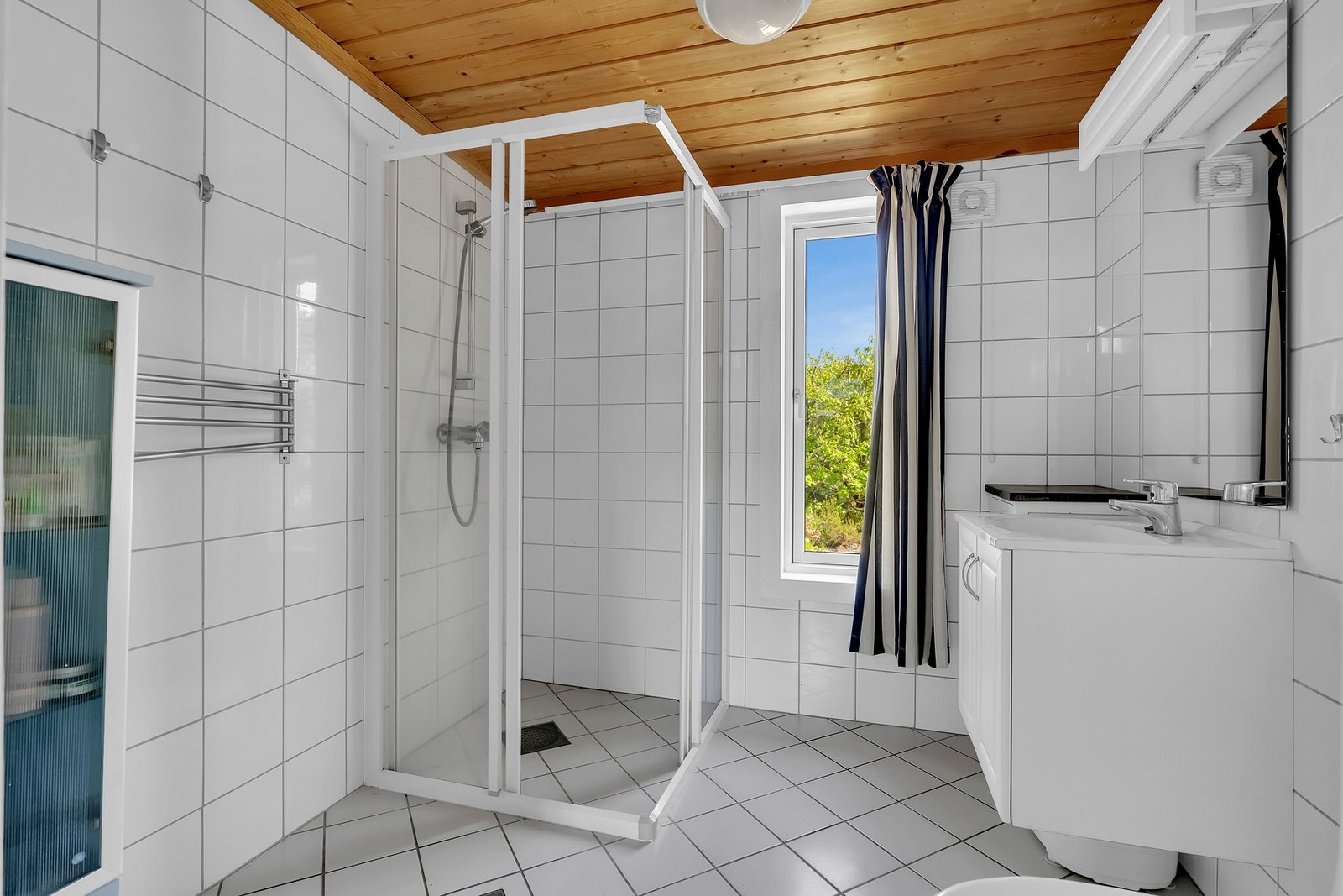 Badet har flislagte gulv og vegger, samt panel i himlingen. Rommet er utstyrt med nedfelt servant i innredning, toalett og dusjhjørne med dusjvegger. Galleribilde