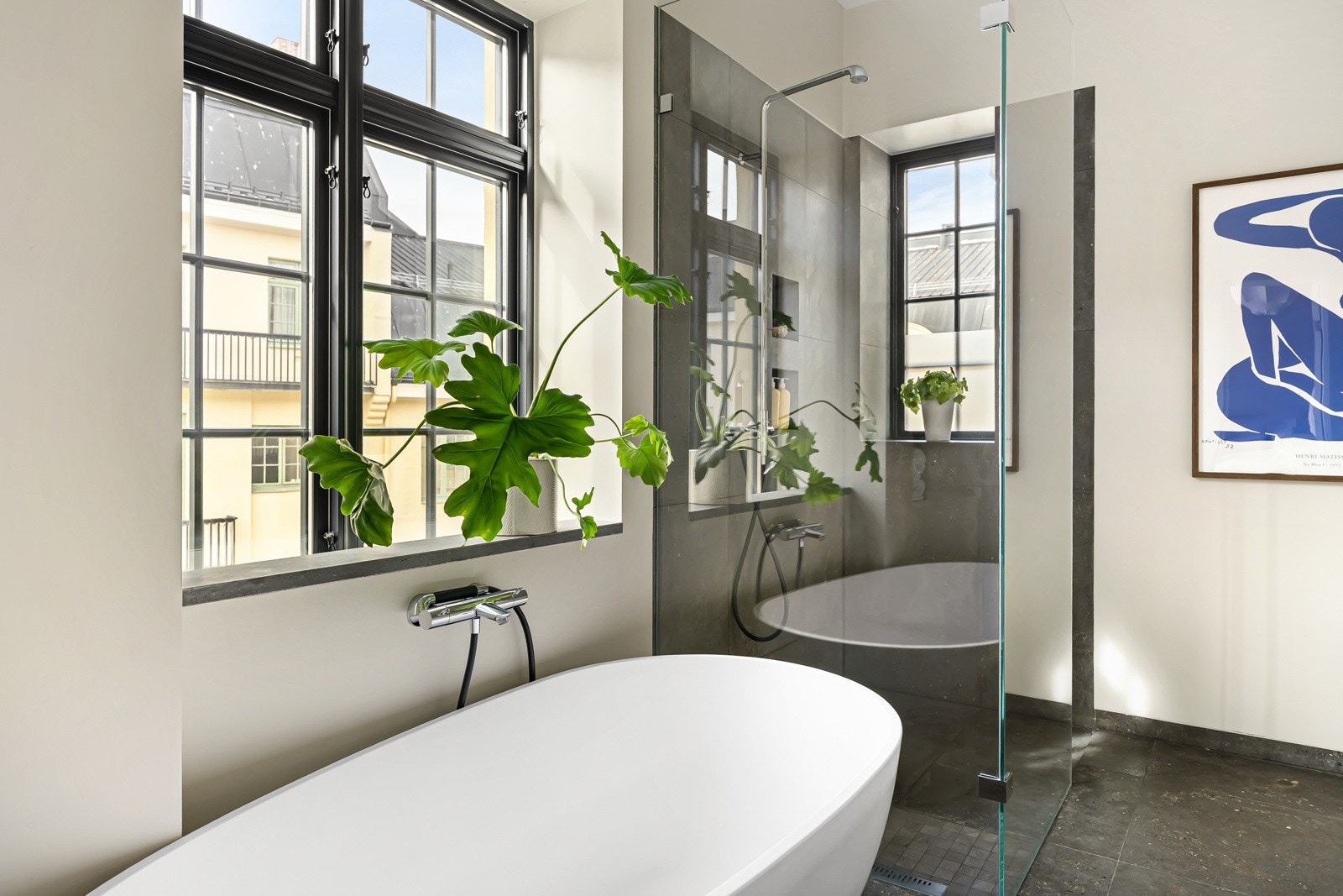 Masse lys fra store vindusflater og lekre, steinmønstrede gulvfliser med varme og et ovalt designbadekar plassert under vinduet. Galleribilde