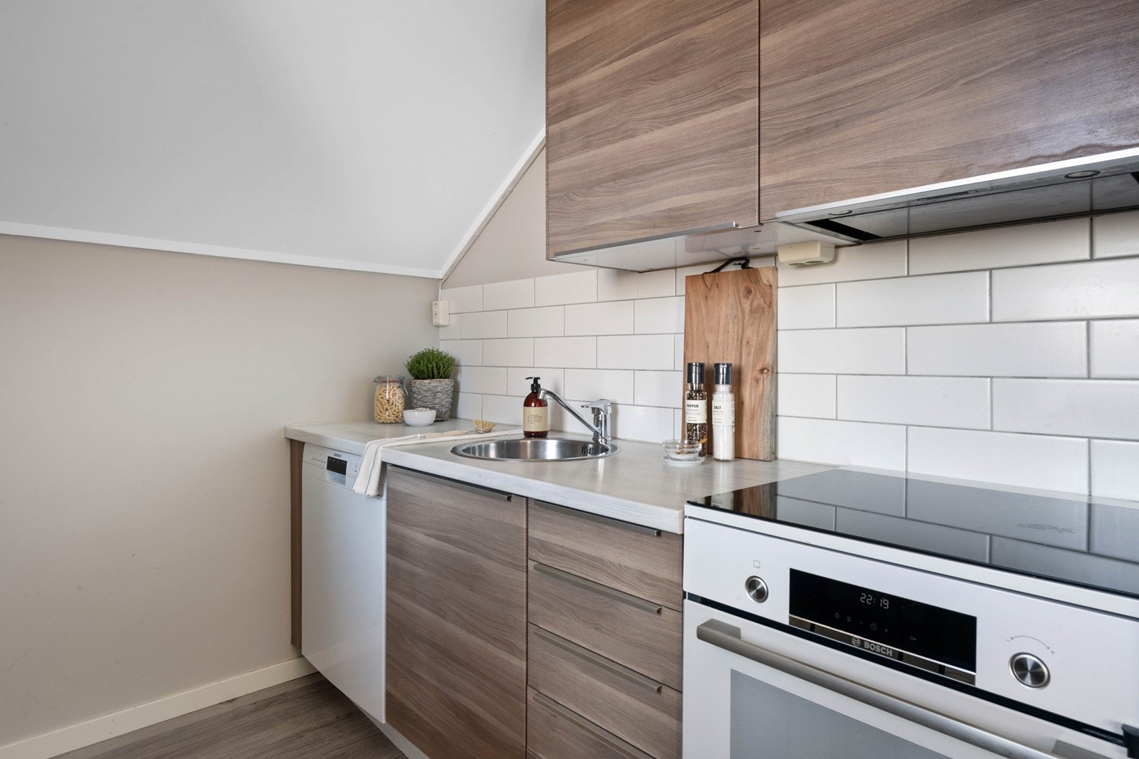 Kjøkkeninnredning bestående av laminat benkeplate, frittstående kjøl/fryseskap, oppvaskmaskin og komfyr. Galleribilde