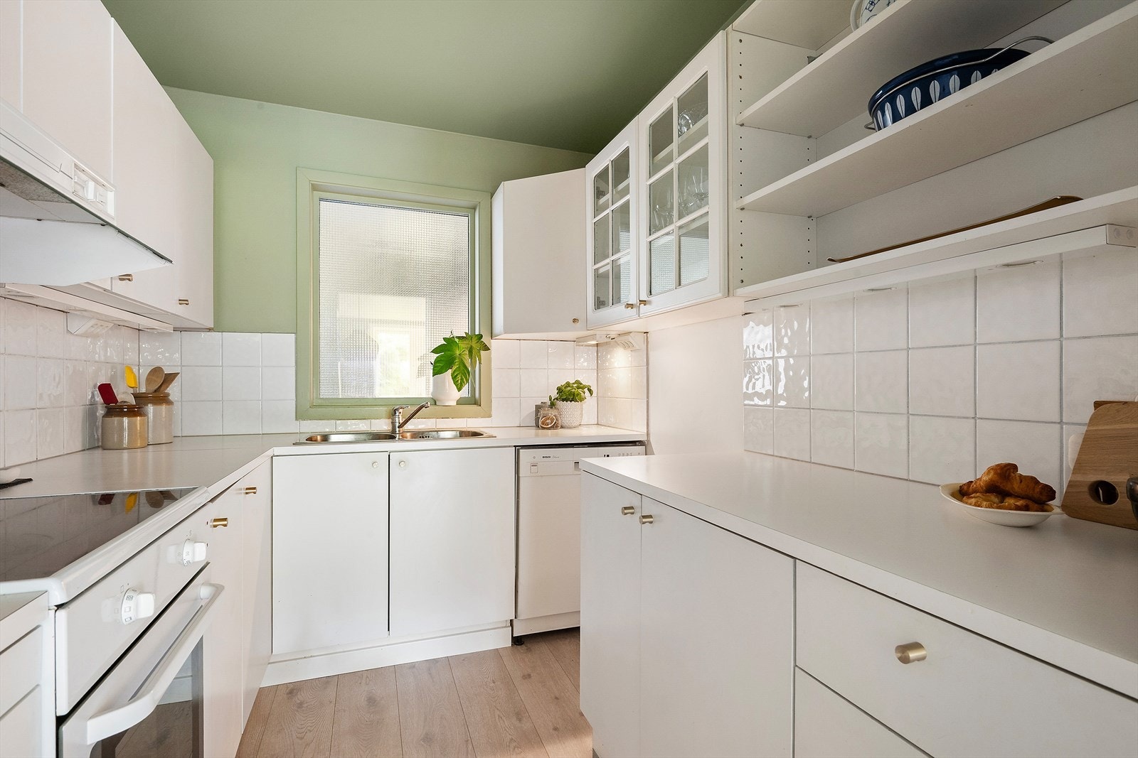 Kjøkkeninnredning med hvite fronter, benkeplater i laminat og fliser på vegg. Opplegg for oppvaskmaskin Galleribilde