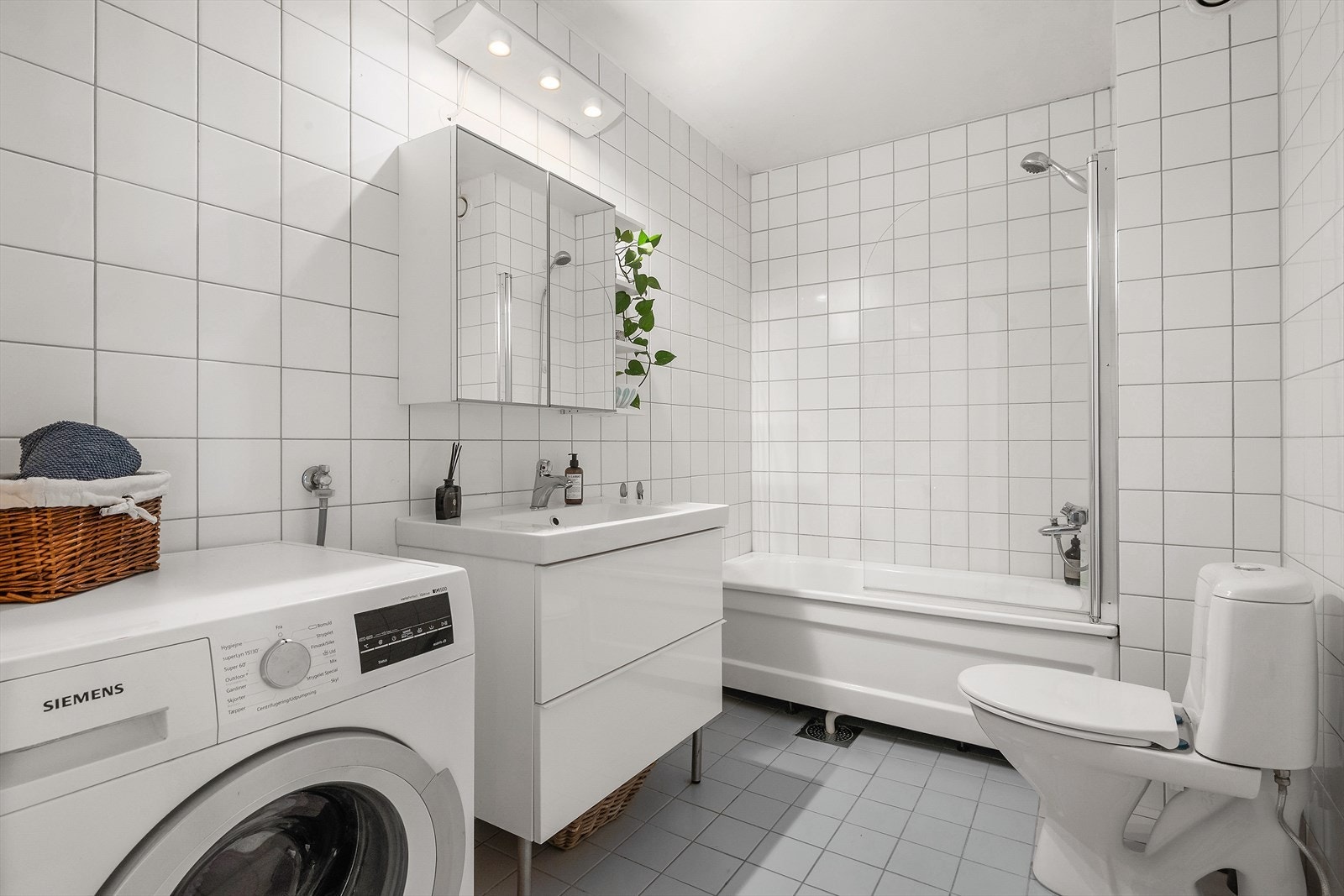 Flislagt bad med varmekabler i gulv opplegg for vaskemaskin. Romslig speilskap, servant med skuffer, badekar og dusj samt toalett Galleribilde