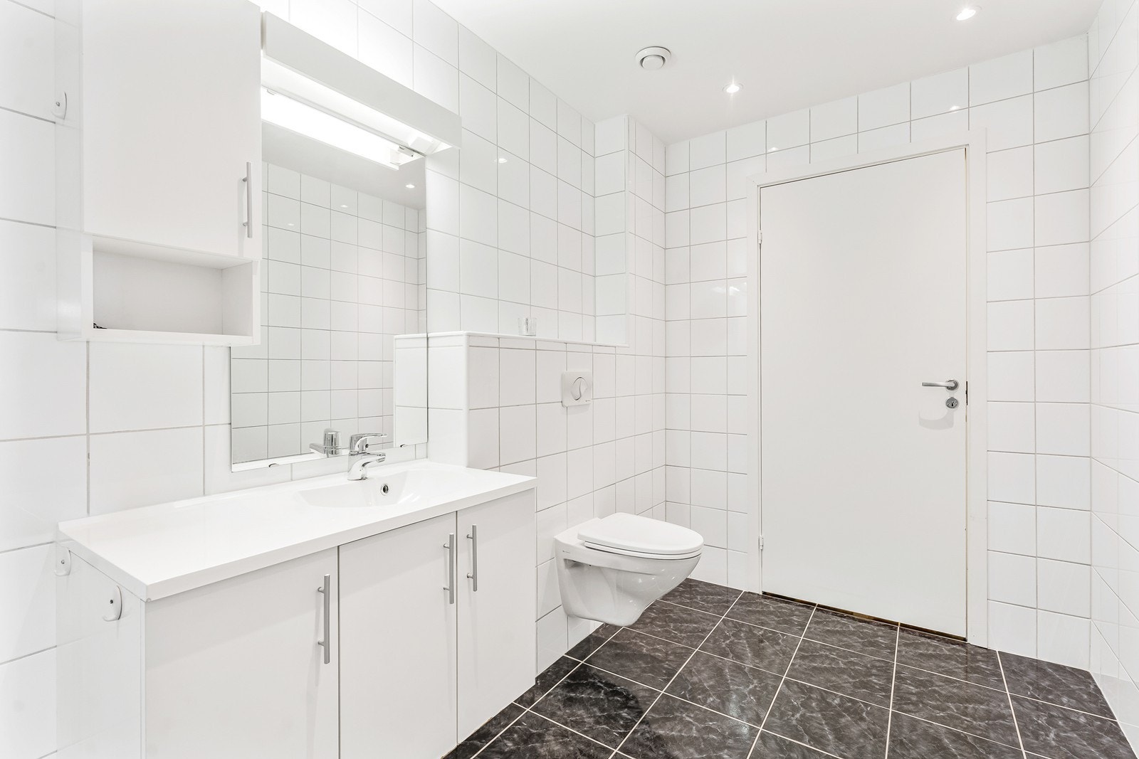 Badet har flislagt vegger/gulv, og en lys skapinnredning med et stort speil. Galleribilde