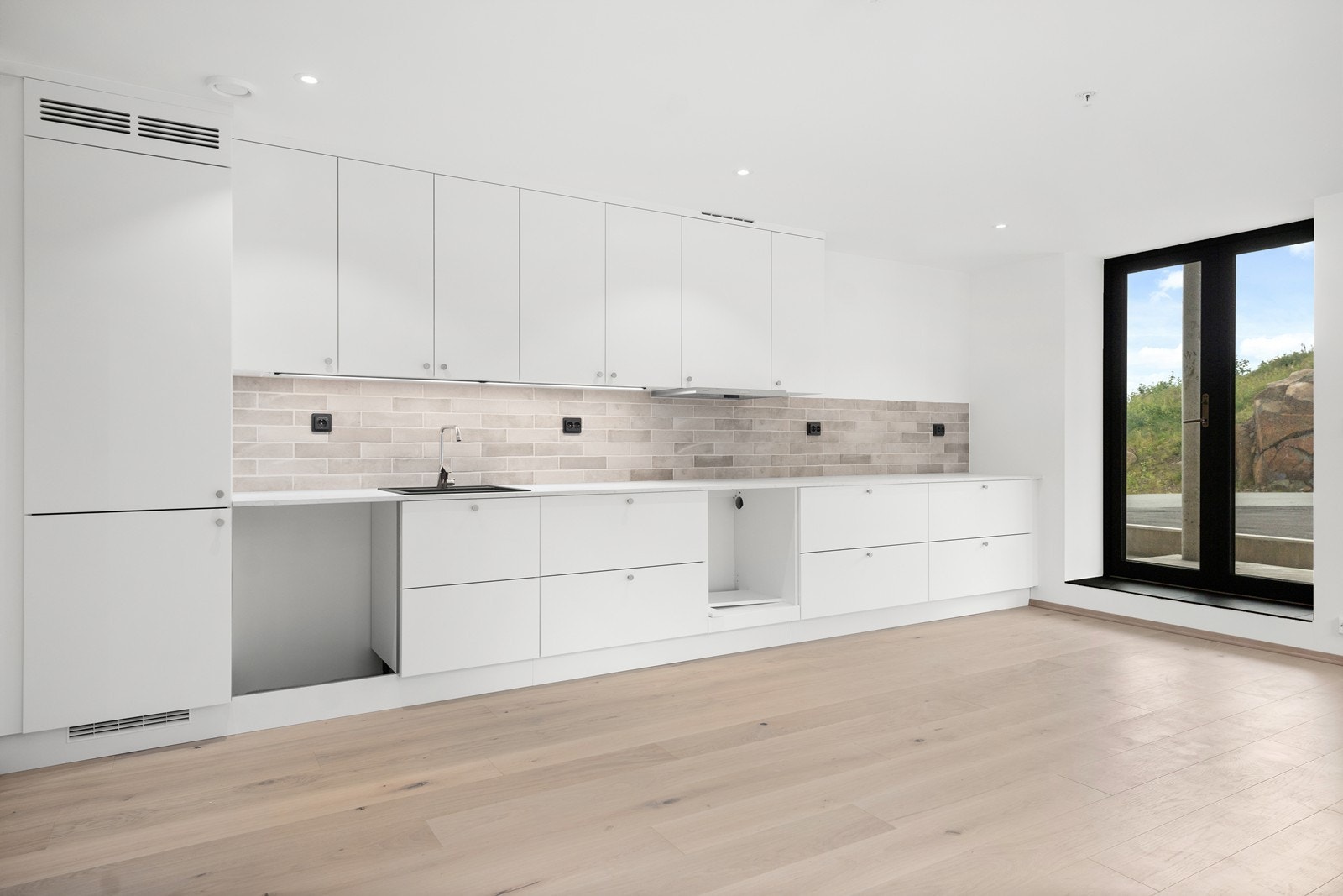 Hvit tidløs kjøkkeninnredning fra Strai kjøkken. Flislagt mellom benkeplate og overskap. Galleribilde