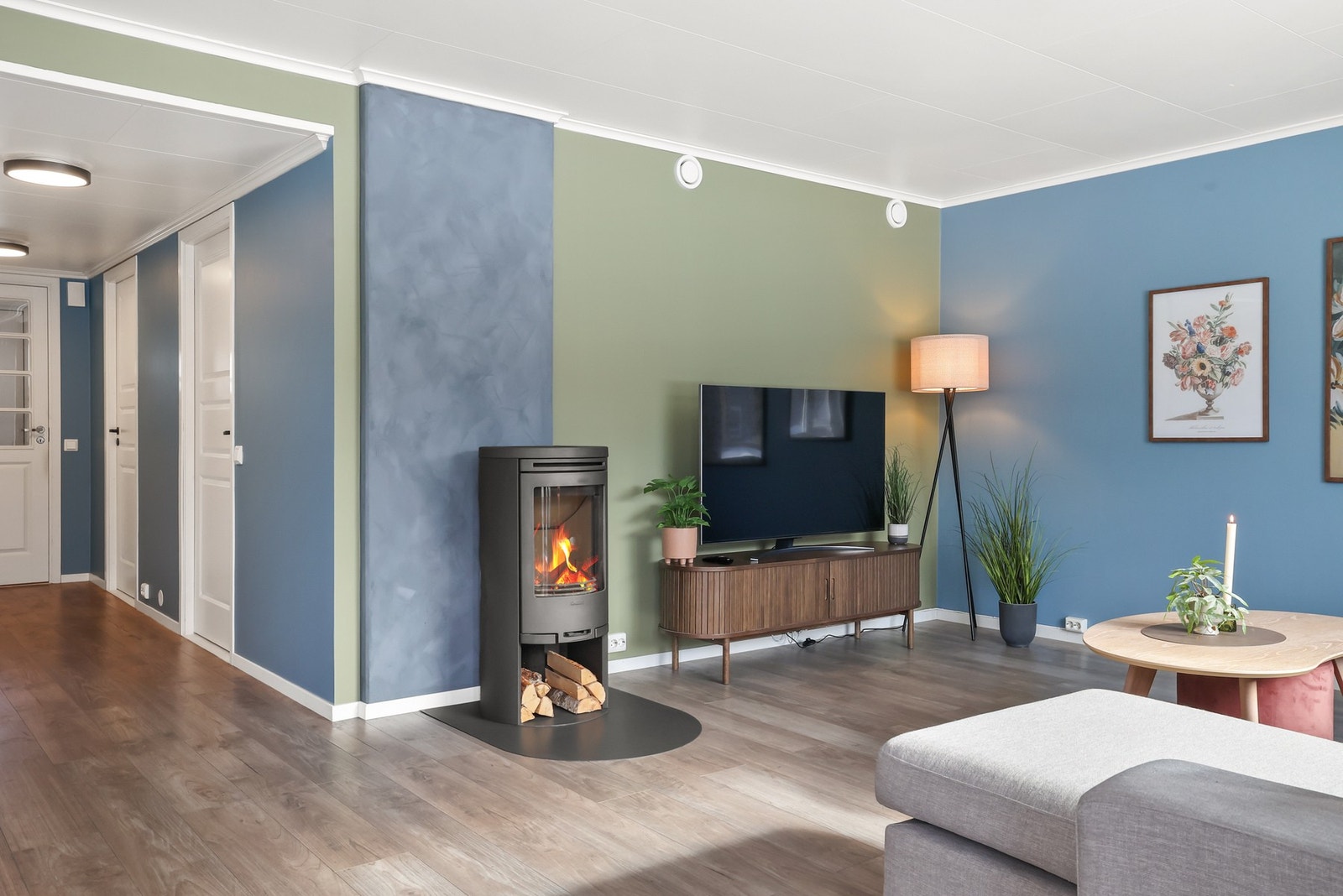 Stuen har et moderne uttrykk med en harmonisk fargepalett i blått og grønt som gir en rolig og stilfull ramme. Galleribilde