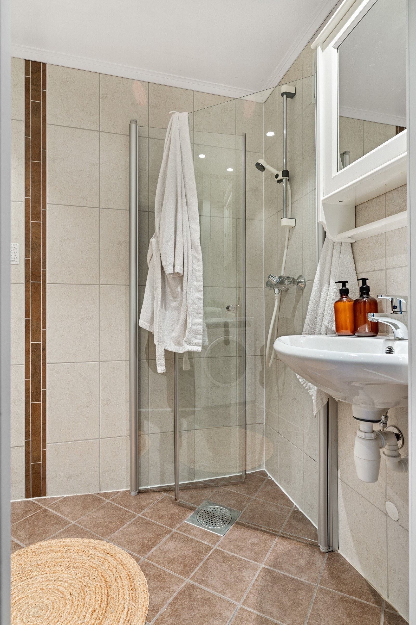 Praktisk baderom med mørkere fliser på gulv og lyser fliser på vegger. Galleribilde