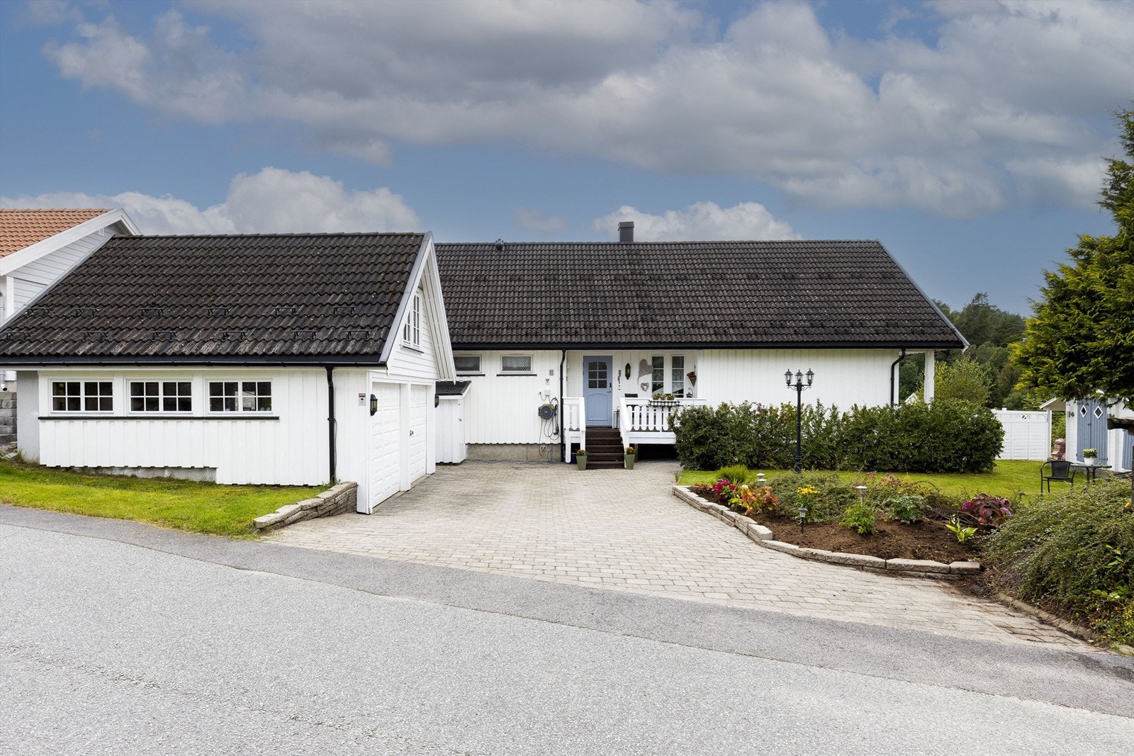 Skrånende tomt opparbeidet med blant annet gårdsplass med belegningsstein, plenarealer og diverse beplantning. Galleribilde
