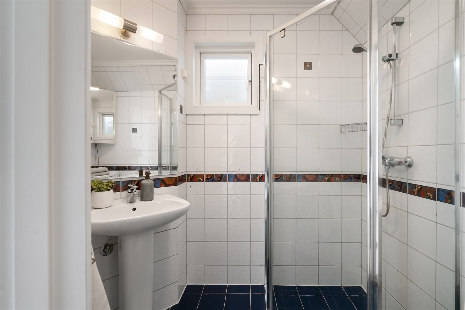 Badet er innredet med dusjhjørne med dører i herdet glass, søyleservant, speil, gulvmontert toalett og opplegg for vaskemaskin. Flislagt gulv med varmekabler, flislagte vegger og malt himling. Galleribilde