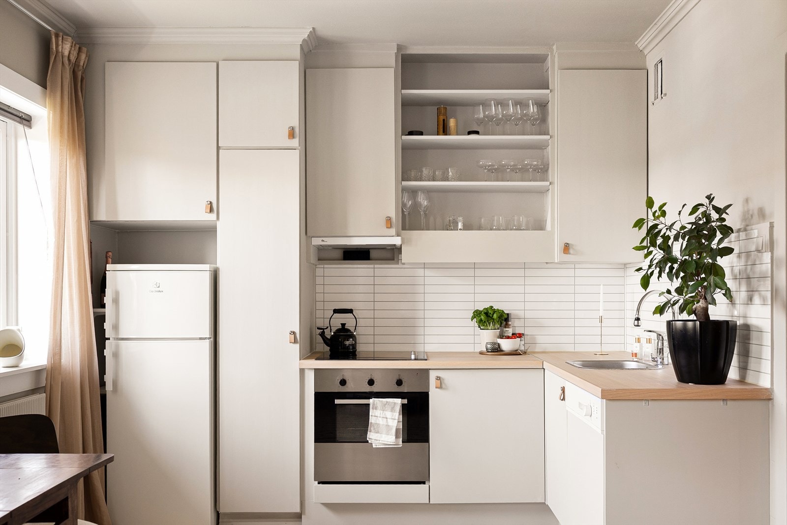 Lys innredning med glatte, malte fronter, laminat benkeplate og flislagte vegger over benkeplaten. Galleribilde