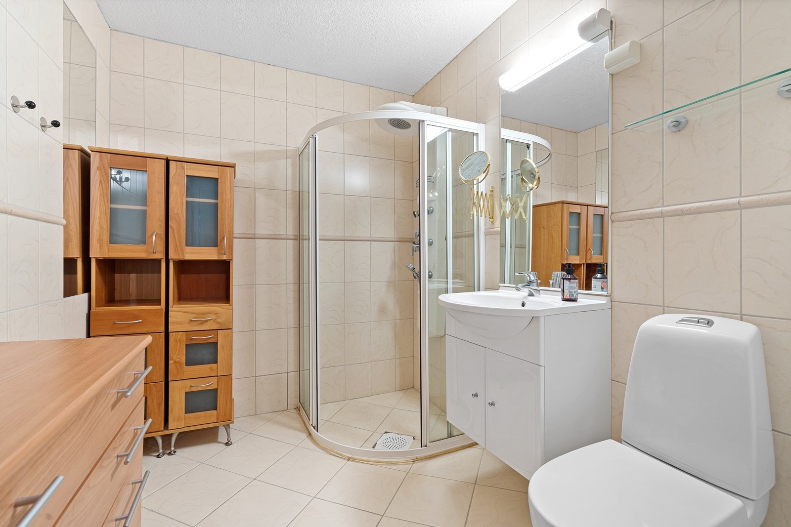 Badet er helfliset med varme i gulvet og inneholder en praktisk dusjnisje, baderomsinnredning, samt toalett. Det er også plass til ekstra kommoder mm. her for ekstra lagringsplass. Galleribilde