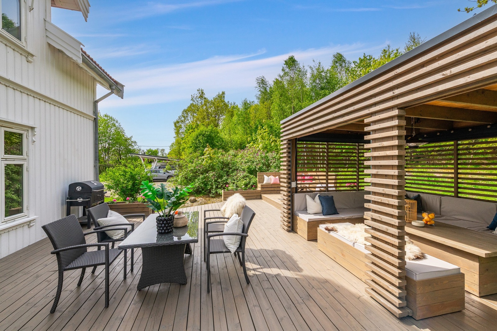 Terrassen har en moderne utforming med terrassebord, blomsterkasser som fungerer som lavt rekkverk, samt en stilfull pergola. Galleribilde
