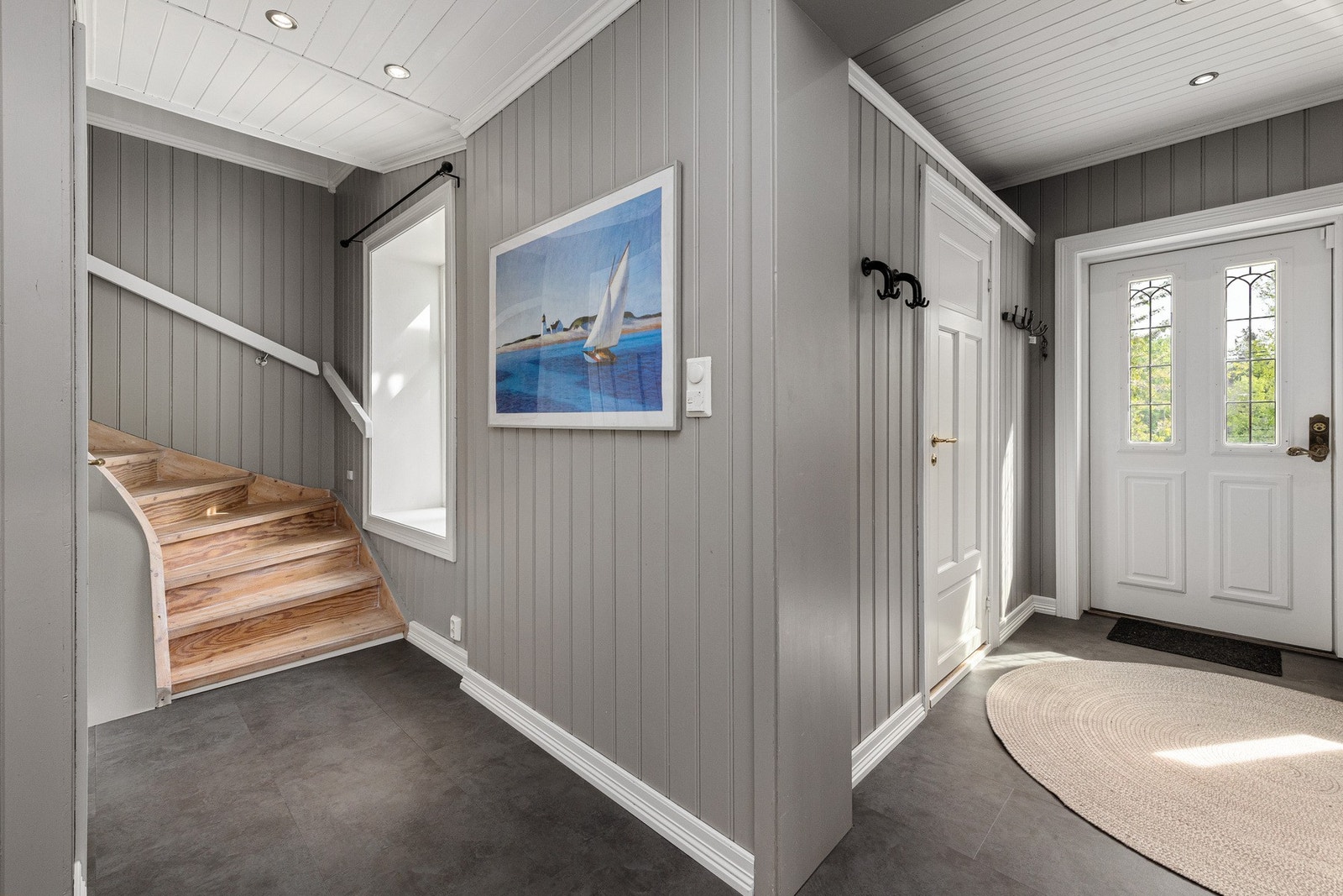 Fra gangen er det adkomst til boligens ulike soner; til venstre åpner det seg en stor stue, rett frem finner du kjøkkenet med utgang til terrasse, mens til høyre ligger både trapp opp til andre etasje og et separat toalettrom. Galleribilde