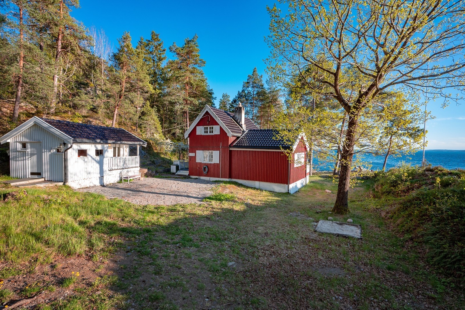 På nordsiden av hytta er en gruset gårdsplass for parkering og et anneks. Galleribilde