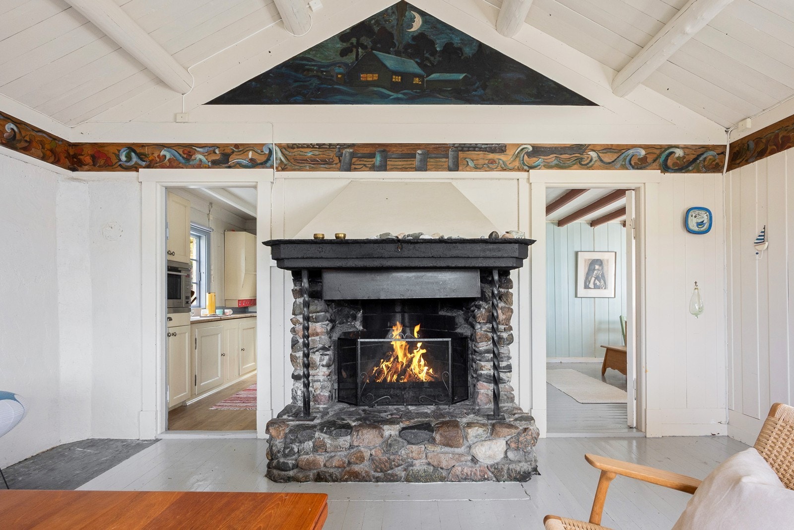 Innenfor kjøkkenet ligger hovedstuen med en fremtredende åpen peis og håndmalte partier. Galleribilde