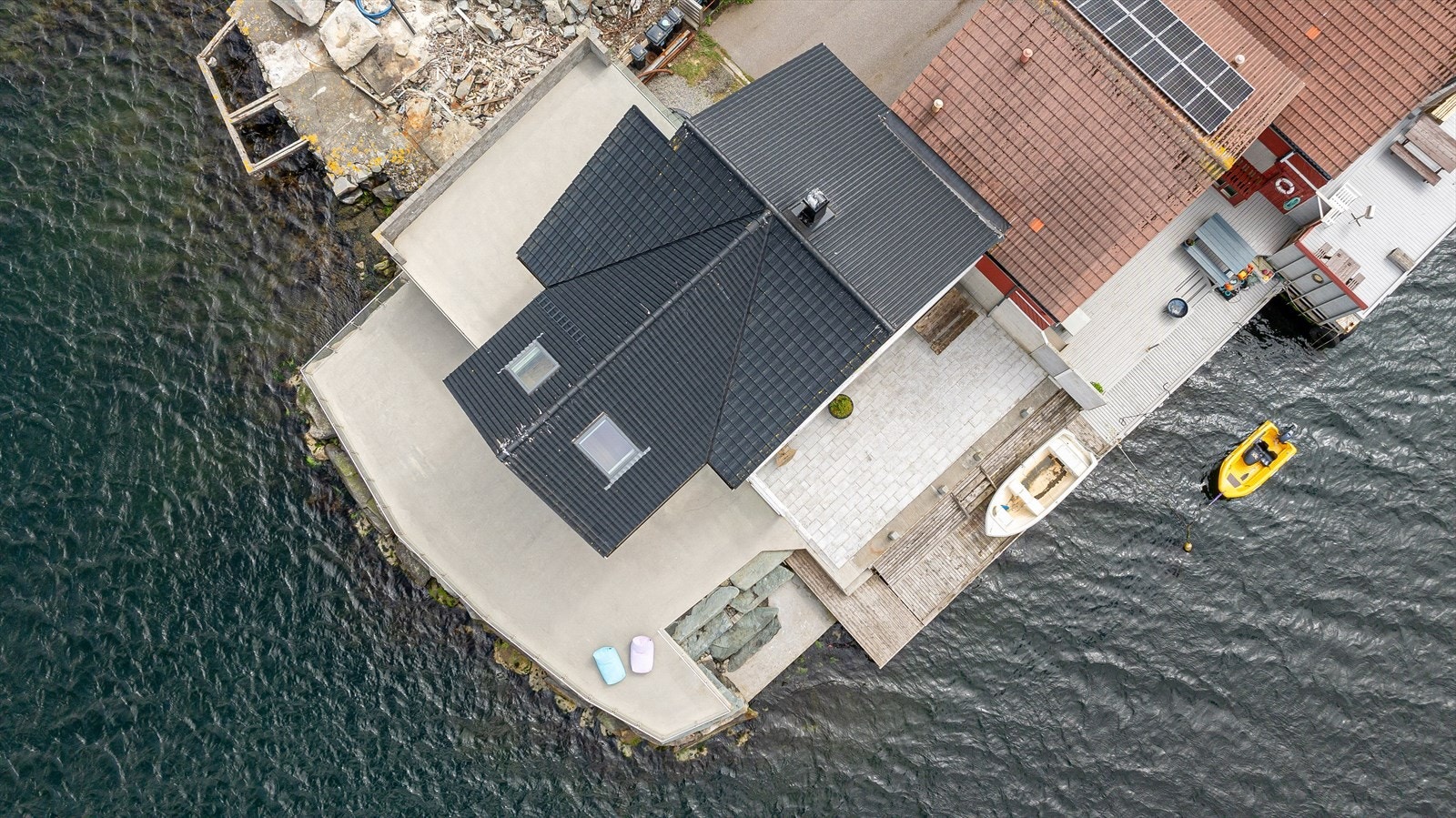 Tomten er pent opparbeidet med singel på parkeringsplass/carport, stor betongterrasse med glassrekkverk mot nord og delvis mot vest, steinbelagte terrasse mot vest og trebrygge mot vest med gode dybdeforhold Galleribilde