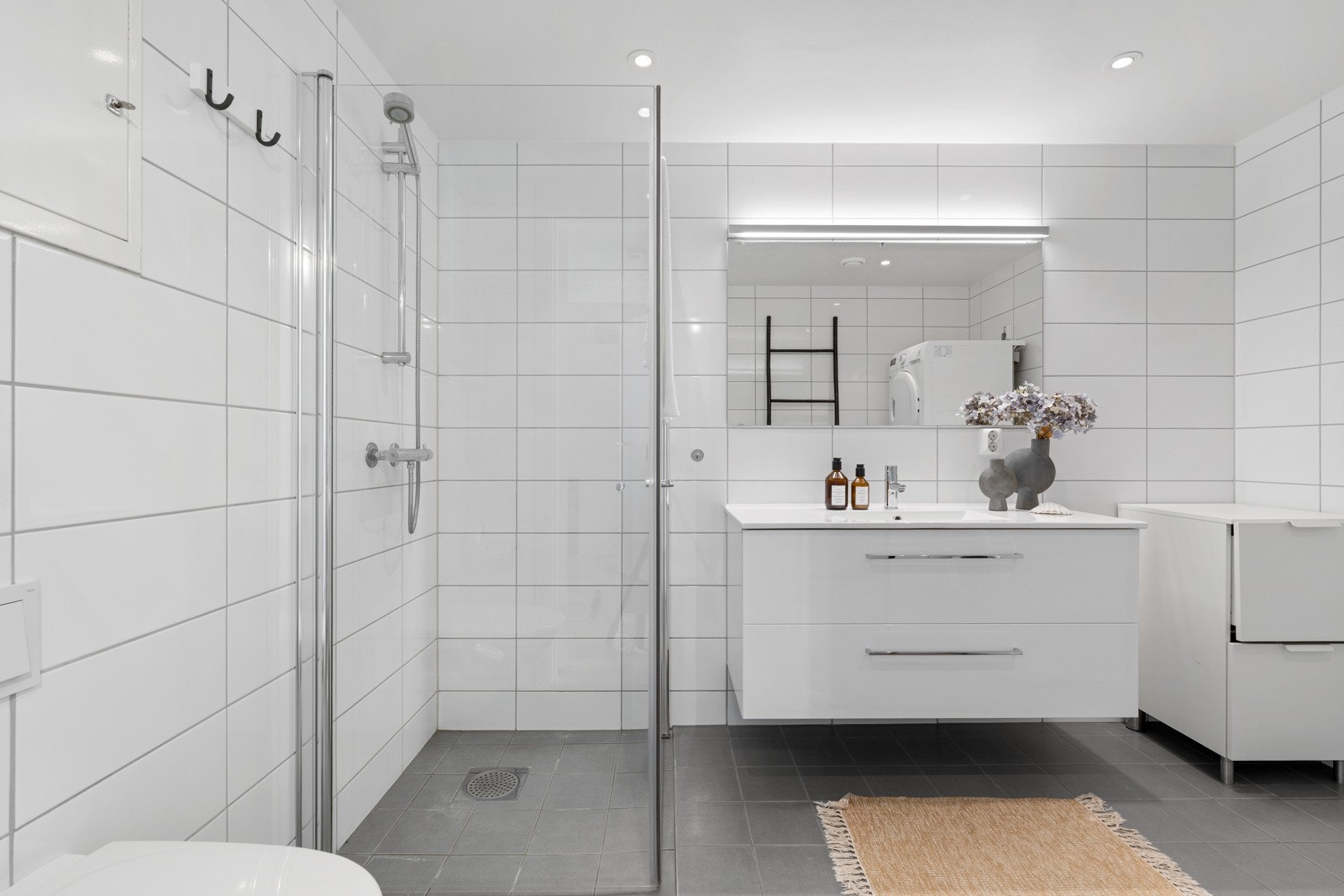 Badet har gulvvarme, spotter i tak og er innredet med servant, møbler, dusjdører, veggmontert wc og opplegg for vaskemaskin Galleribilde