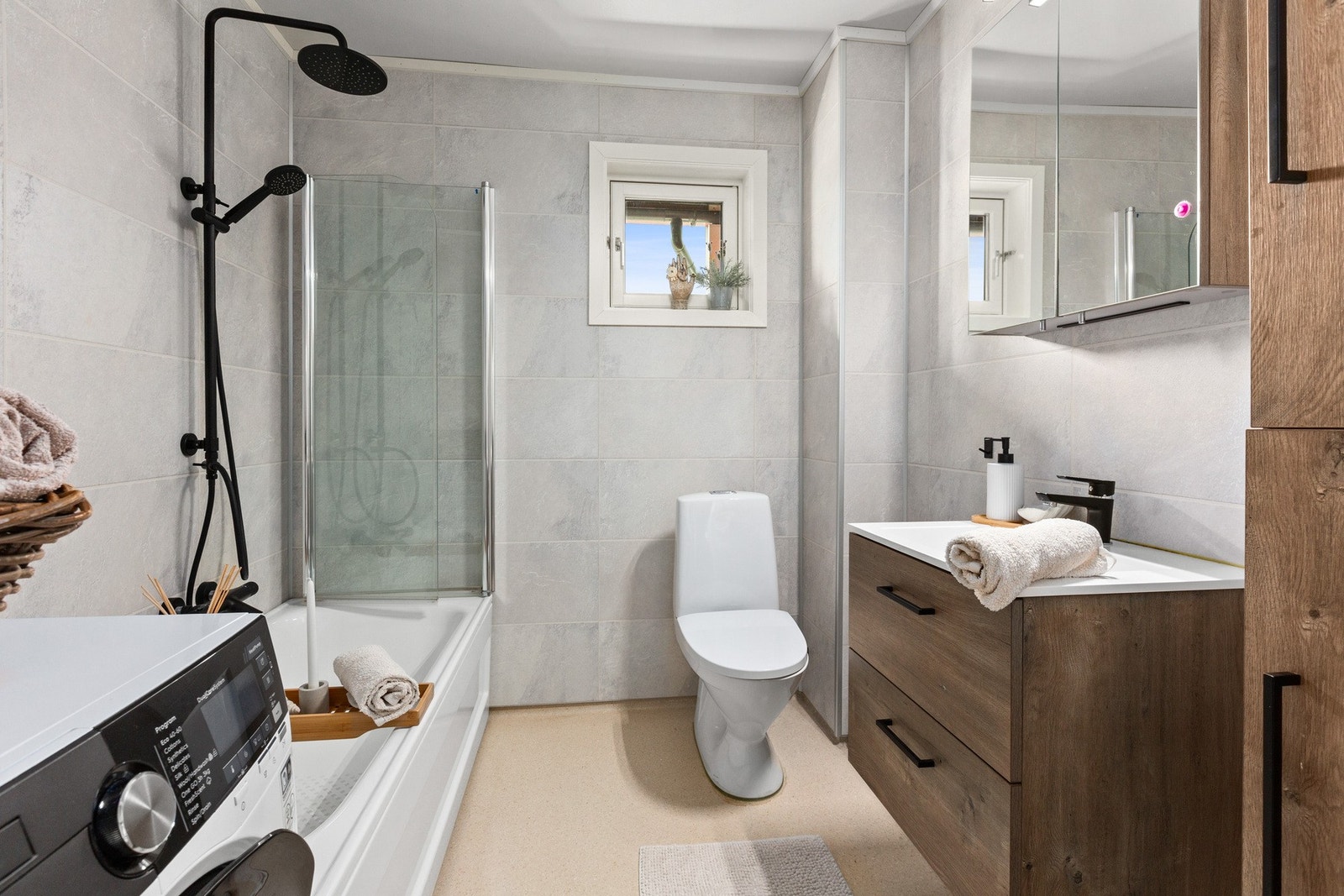 Badet fremstår moderne og romslig. Badekaret er utstyrt med dusjdører, slik at det enkelt kan benyttes som en fullverdig dusjløsning. Galleribilde