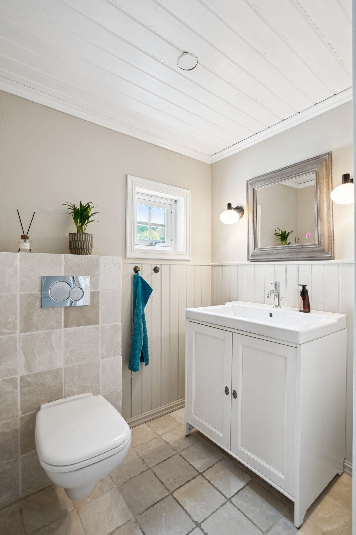 Pent toalettrom med marmorfliser og gulvvarme. Vegger med fliser, panel og tapet. Veggengt toalett og servantskap med porselens servant. Galleribilde