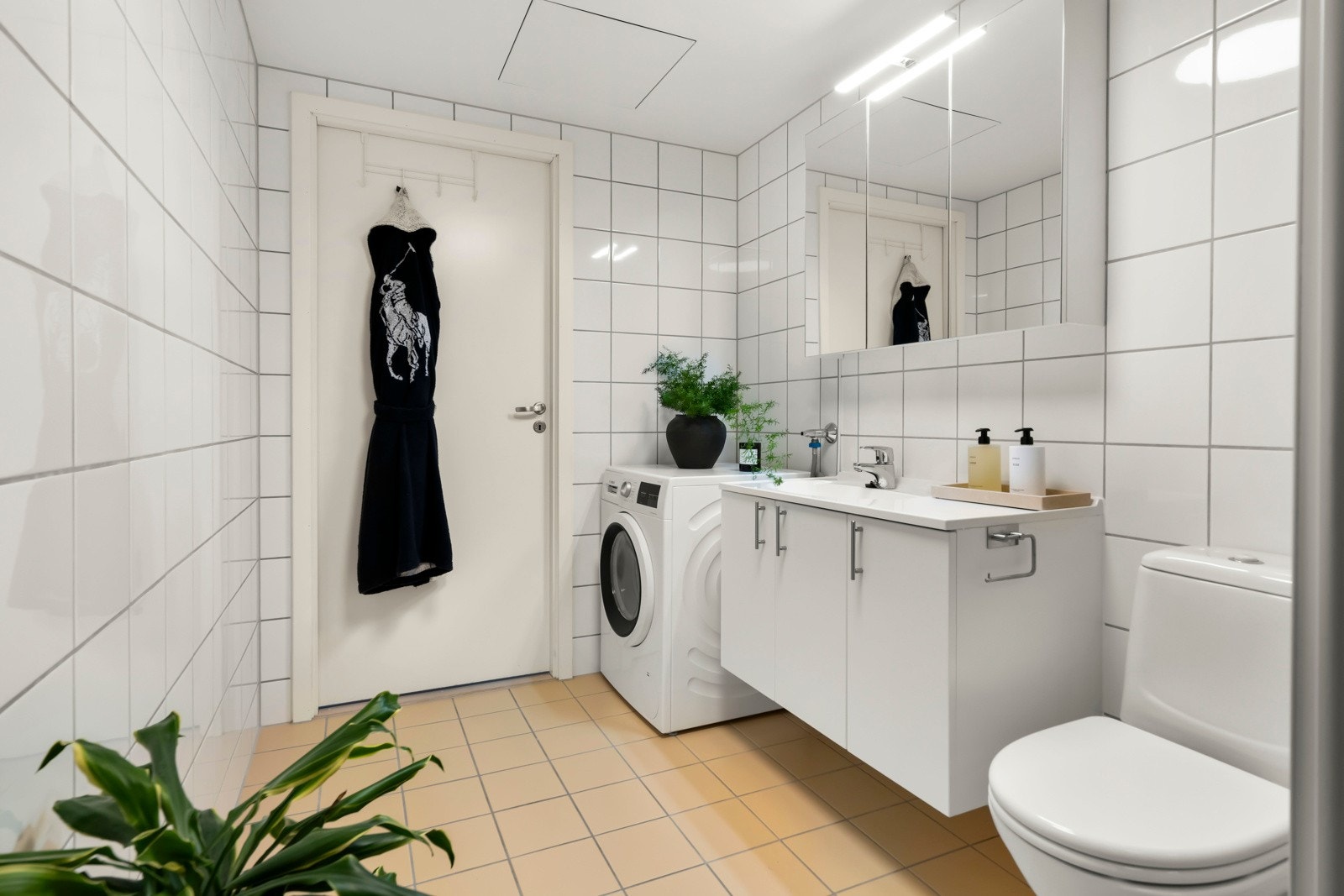 Baderomsinnredningen byr på servantskap med glatte, folierte fronter og heldekkende servant, samt speilskap med lysarmatur på vegg over servant. Videre er det dusjhjørne og toalett. Galleribilde