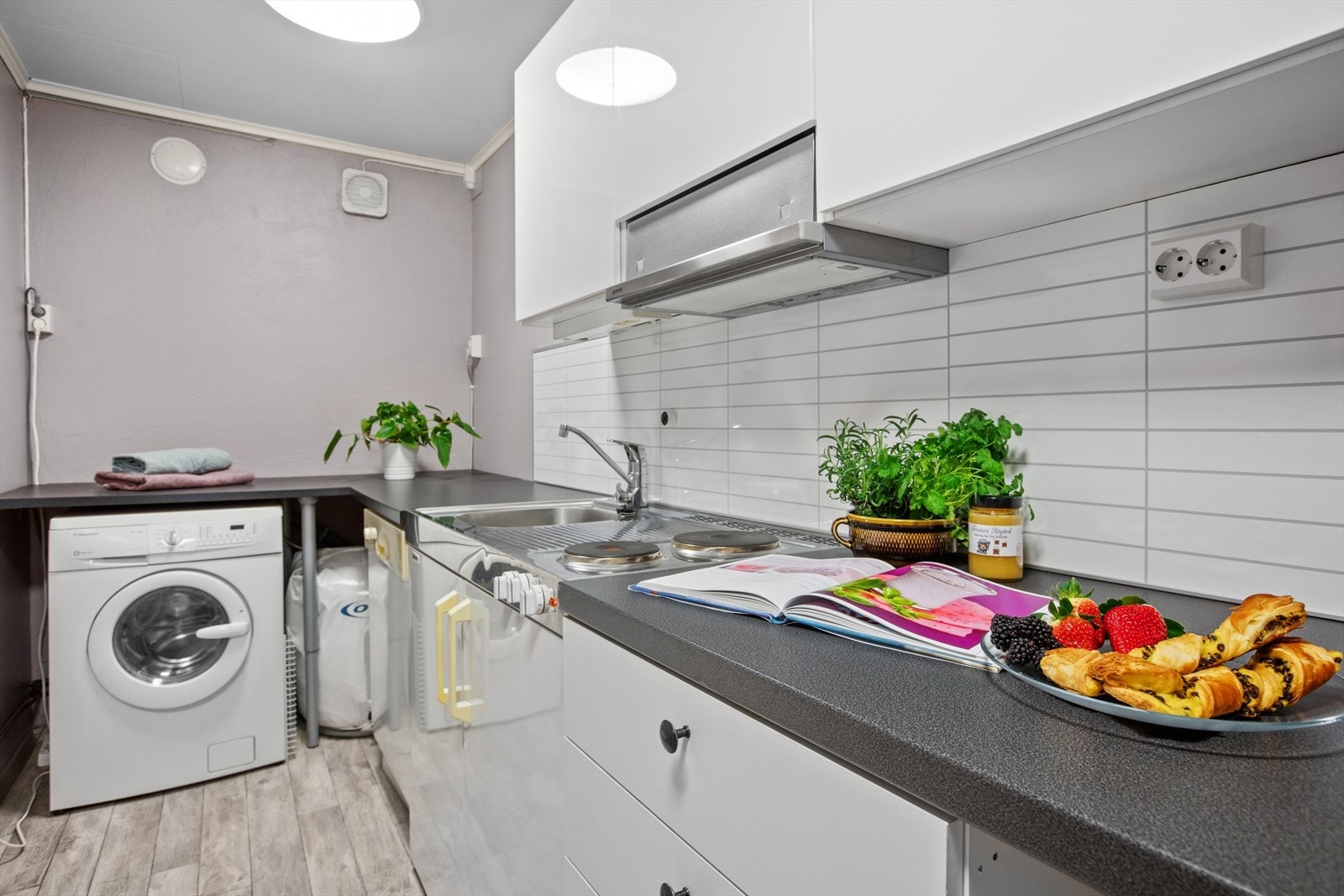 Hybelkjøkken i underetasje med hvite glatte fronter og laminert benkeplate. Inneholder oppvaskmaskin, vaskemaskin og to keramiske topper samt integrert kjøleskap. Galleribilde