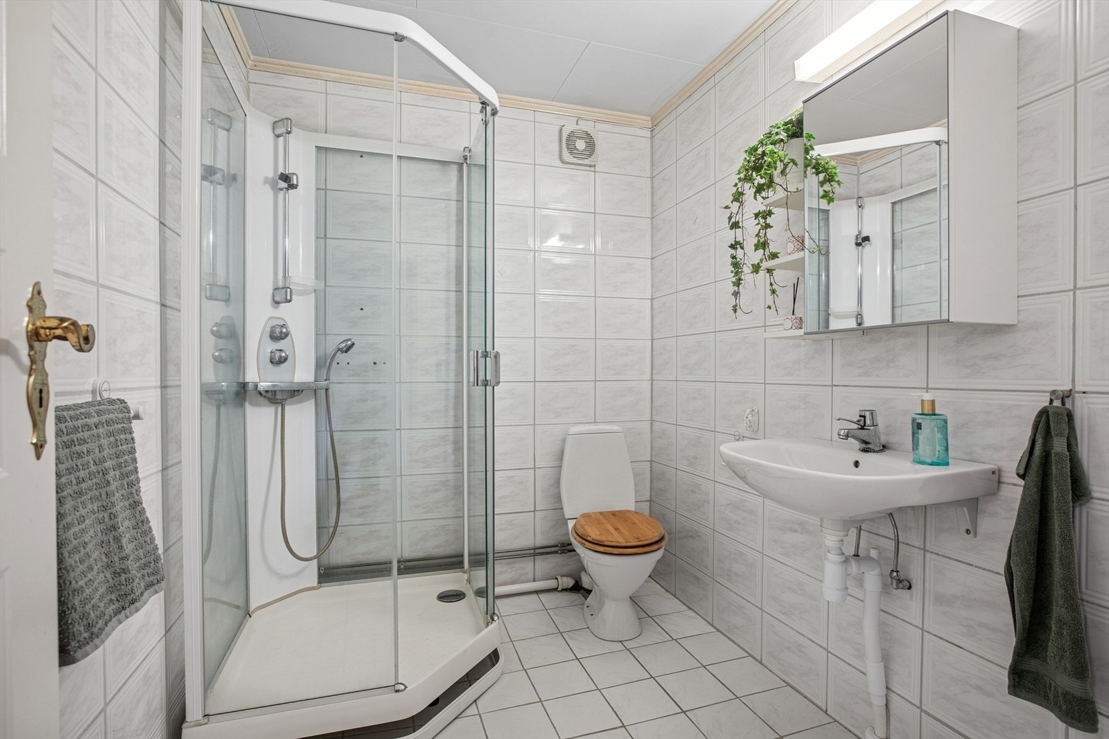 Baderom med fliser på vegger og gulv. Badet har baderomsinnredning med servant, gulvstående toalett og dusjkabinett. Galleribilde