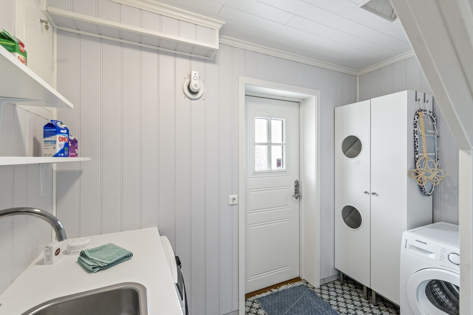 Praktisk vaskerom med egen utgang. Her er det gode oppbevaringsmuligheter, opplegg til vaskemaskin og plass til tørketrommel samt utslagsvask med benkeplate. Galleribilde