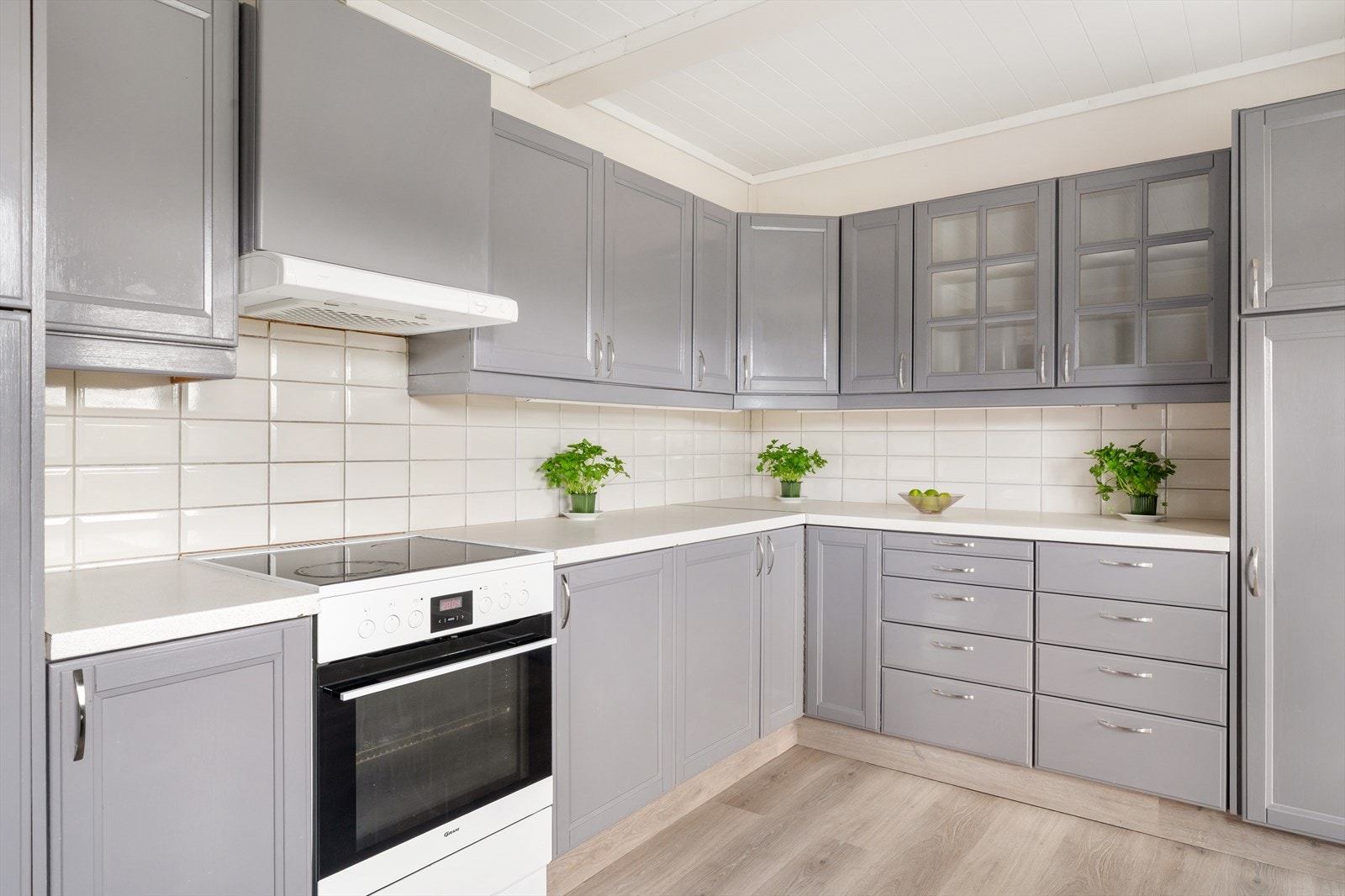 Velholdt kjøkkeninnredning med malte, profilerte fronter og fliser på vegg mellom disk og overskap Galleribilde