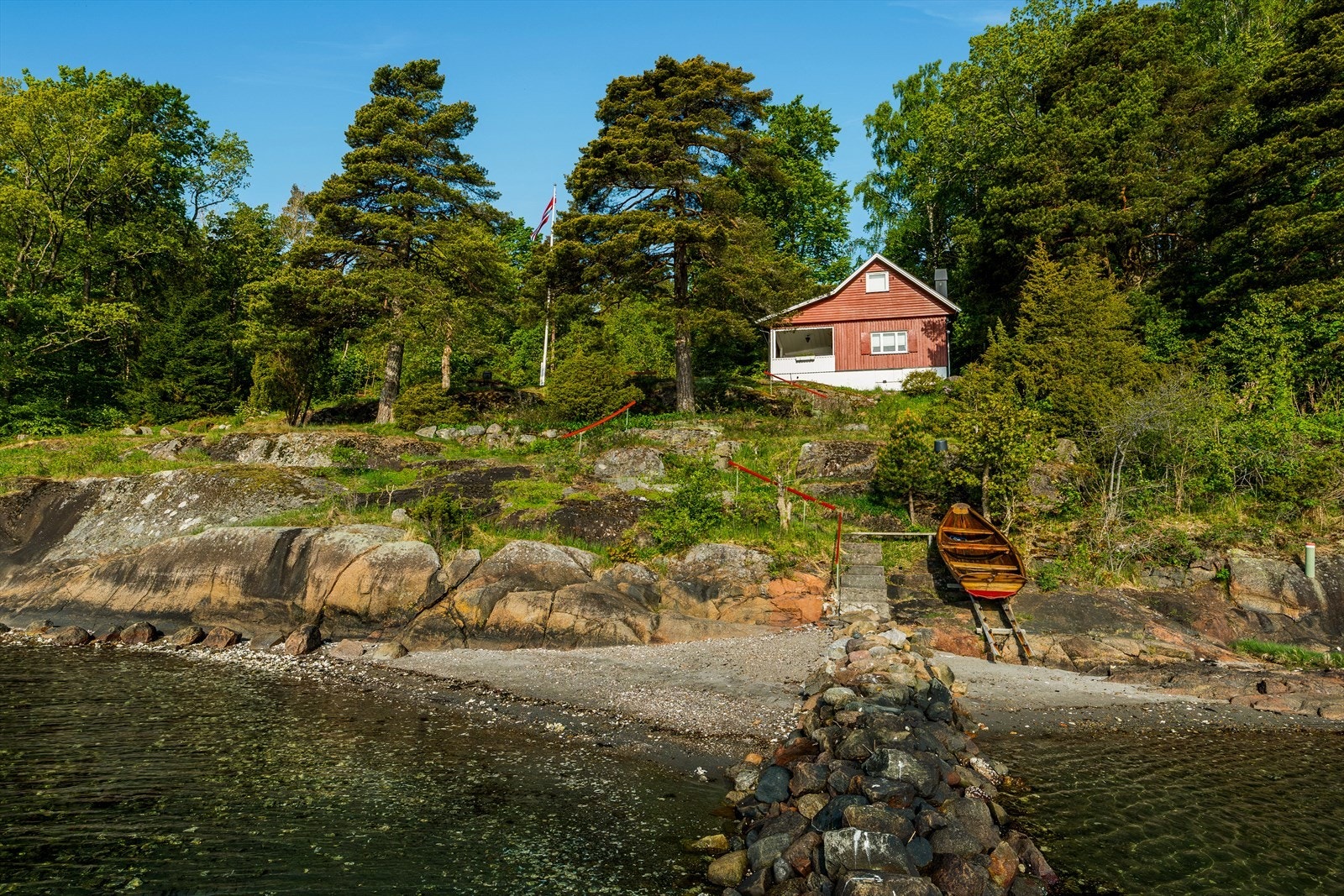 Hytta ligger på en høyde, og fra hagen er det laget trapp i terrenget ned til strandlinjen. Galleribilde