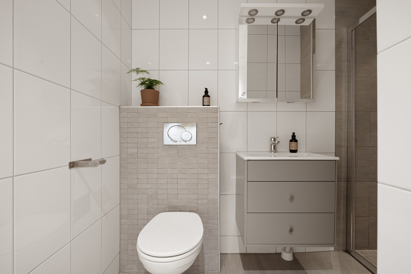 Moderne baderomsinnredning med skuffer og heldekkende servant, speilskap med belysning over. Galleribilde