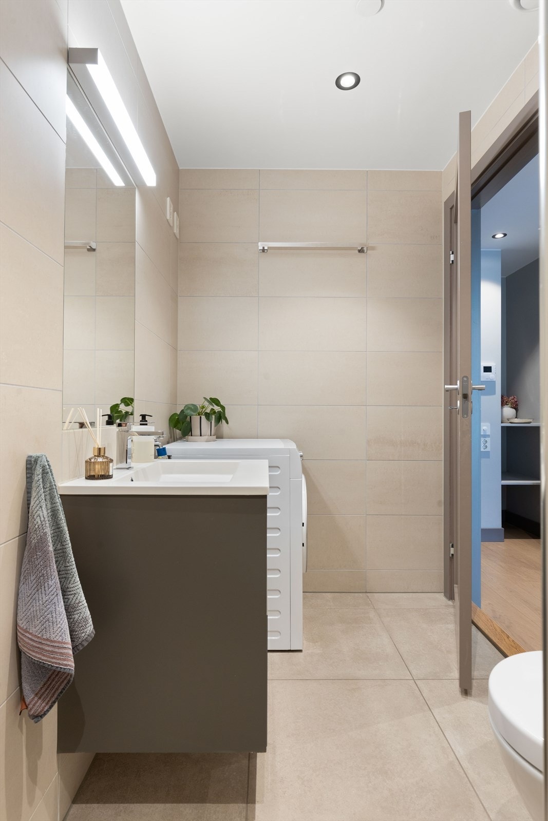 Badet er utstyrt med et veggmontert toalett, servant, dusjnisje med glassdører og opplegg for vaskemaskin. Galleribilde