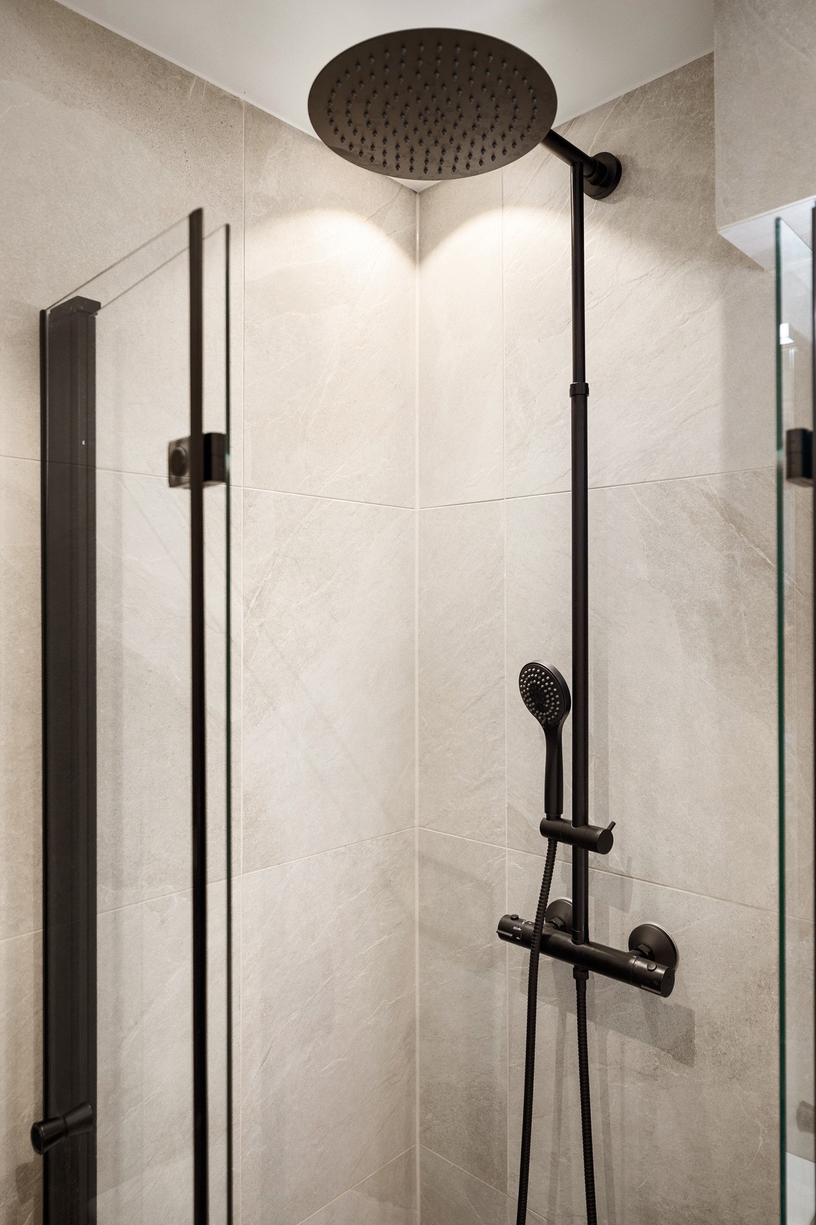 Dusjhjørne med innfellbare dører i glass og stilren dusjgarnityr med regnfallsdusj og hånddusj. Galleribilde