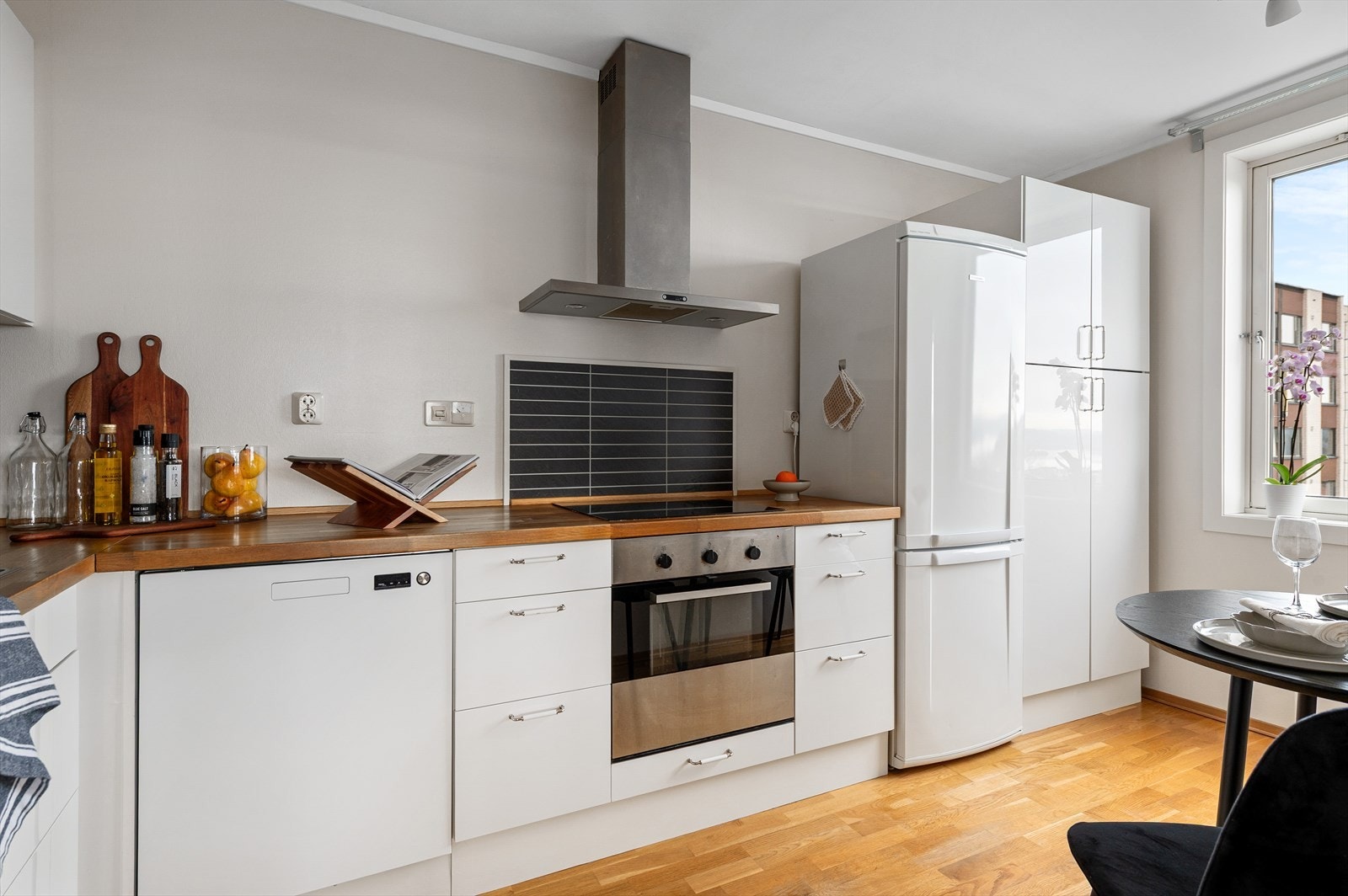 Lyst og innbydende kjøkken med glatte hvite fronter, benkeplate heltre og kitchenboard bak kokesone og vask. Galleribilde