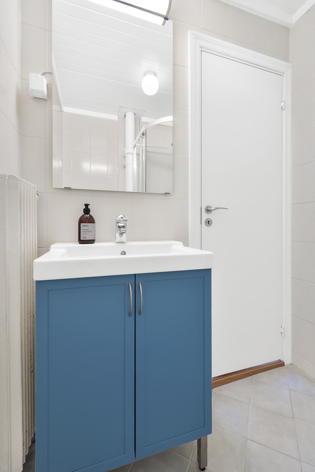 Badet er innredet med dusjkabinett, gulvstående toalett, heldekkende servant på benkeskap og speil med belysning over. Galleribilde