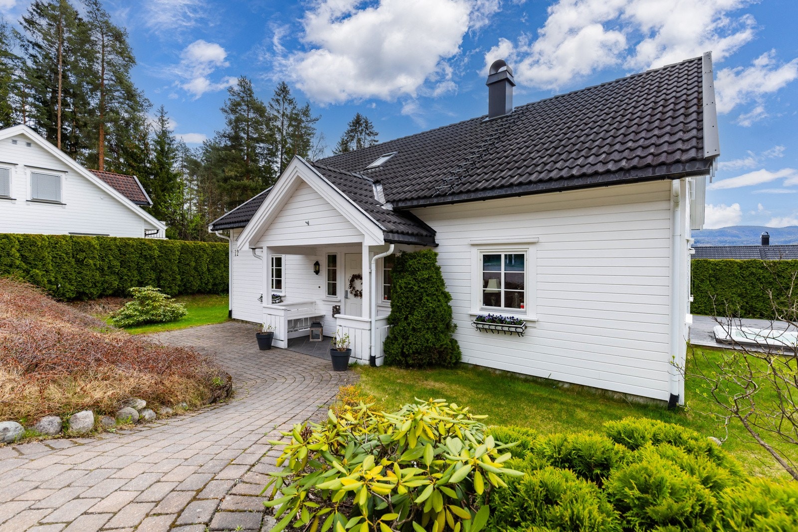 Nærmest flat og pent opparbeidet tomt med innkjøring og gårdsplass belagt med asfalt og belegningsstein, forstøtningsmurer, marterrasse, plenarealer og diverse beplanting Galleribilde