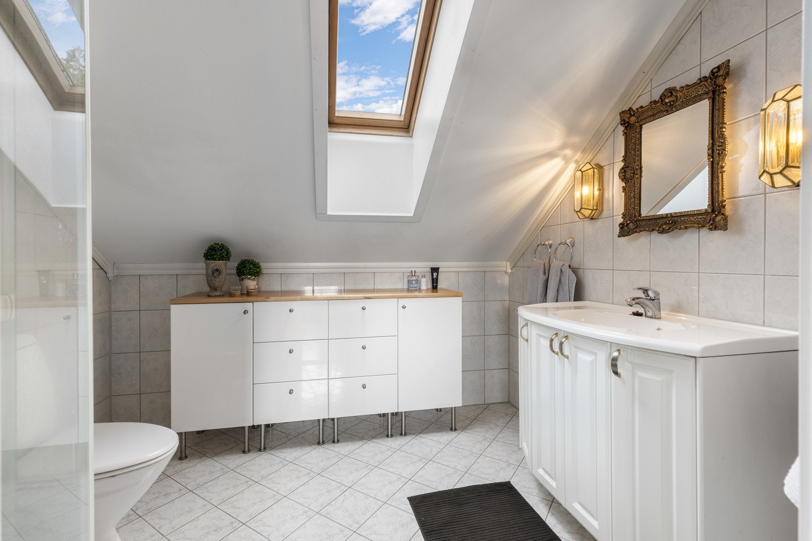 Pent flislagt bad i andre etasje med varmekabler i gulv. Badet er innredet med dusjhjørne med skyvedør av glass, toalett, seksjon med skap og servant Galleribilde