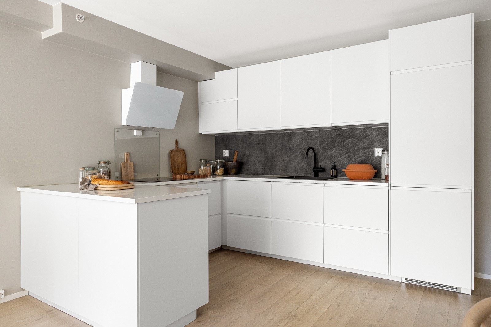 Lys laminat benkeplate med nedfelt komposittvask og ett-greps armatur i sort gir en fin kontrast. Kjøkkenet er utstyrt med integrerte hvitevarer fra Ikea, herunder oppvaskmaskin, kjøl/frys, stekeovn, platetopp og veggmontert avtrekksvifte. Galleribilde