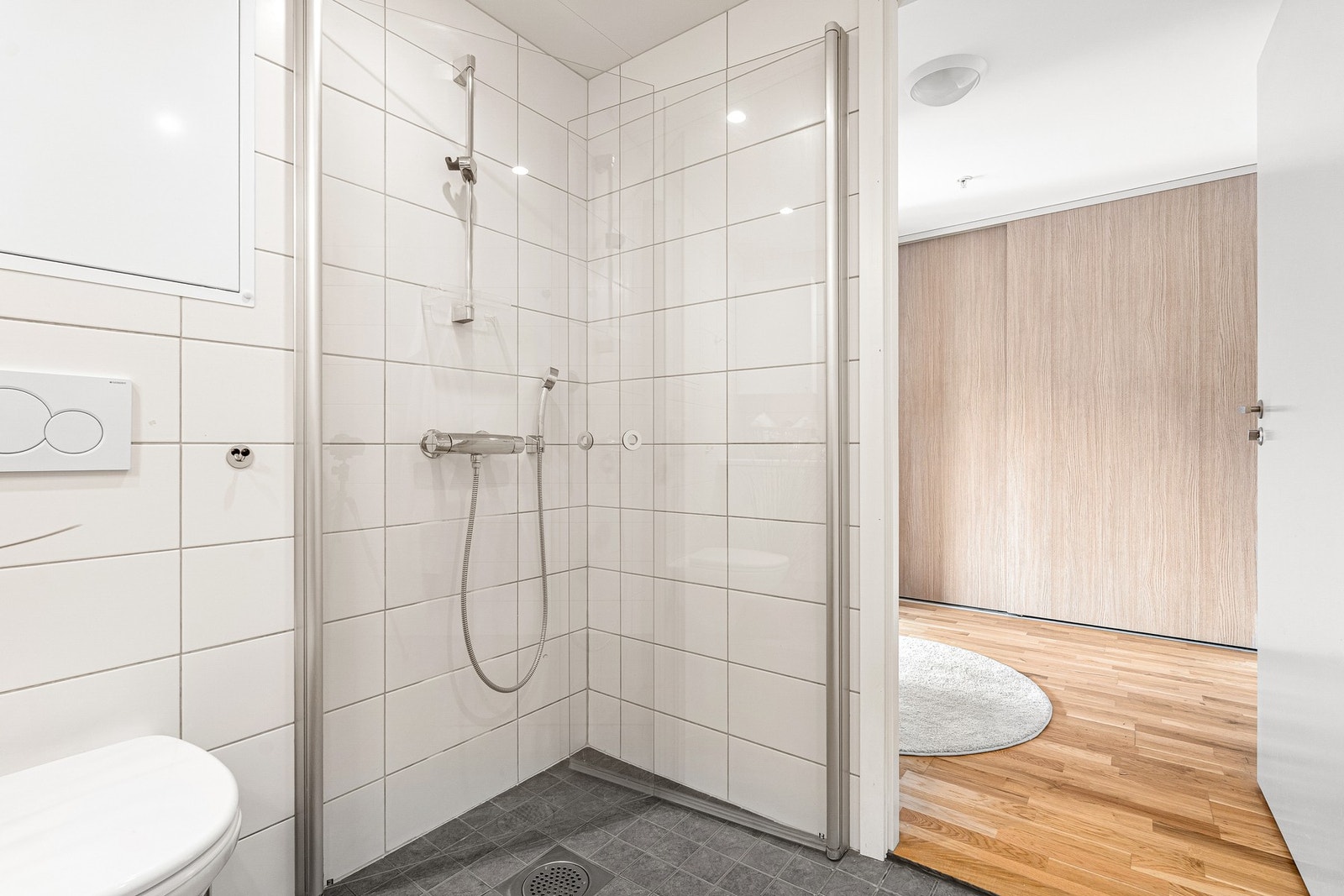 Badet er utstyrt med plassbesparende dusjdører i glass, vegghengt toalett og kran/avløp for vaskemaskin. Galleribilde